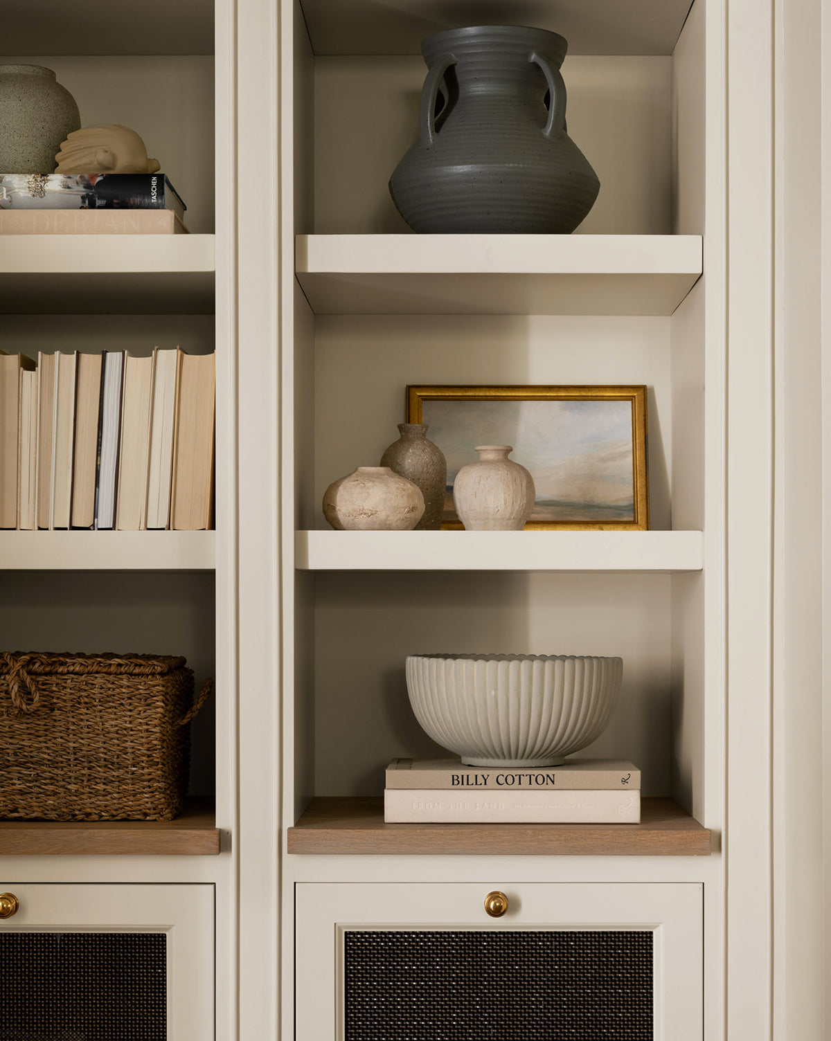 A green-tinted beige built-in bookshelf showcases vases, a landscape painting, neatly stacked books, a woven basket, and the Reeded Bowl with a scalloped rim placed on top of two books.