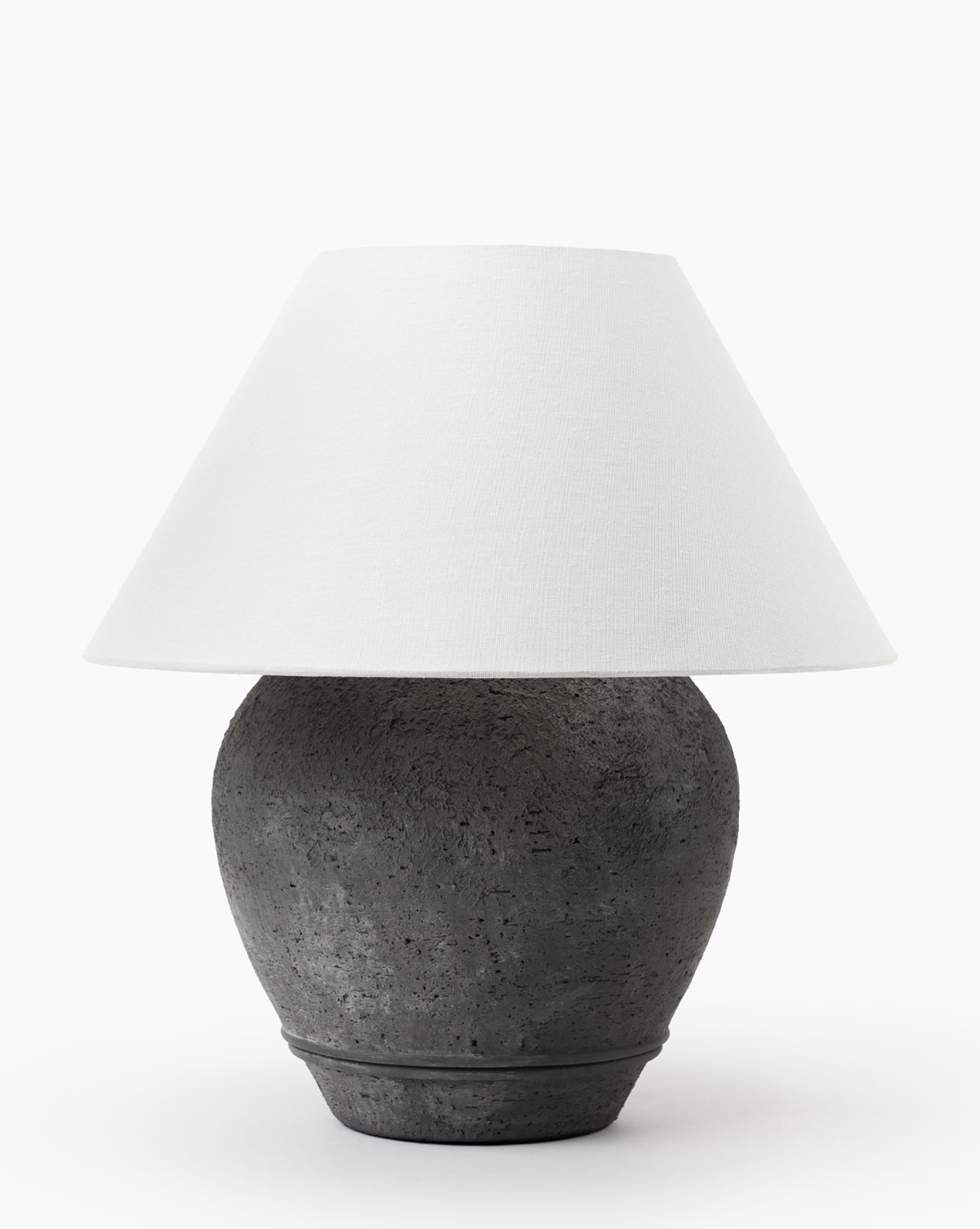 The Abbott Ceramic Table Lamp features a textured dark gray round ceramic base and a wide white linen shade, shown against a plain white background, by Vendixs
