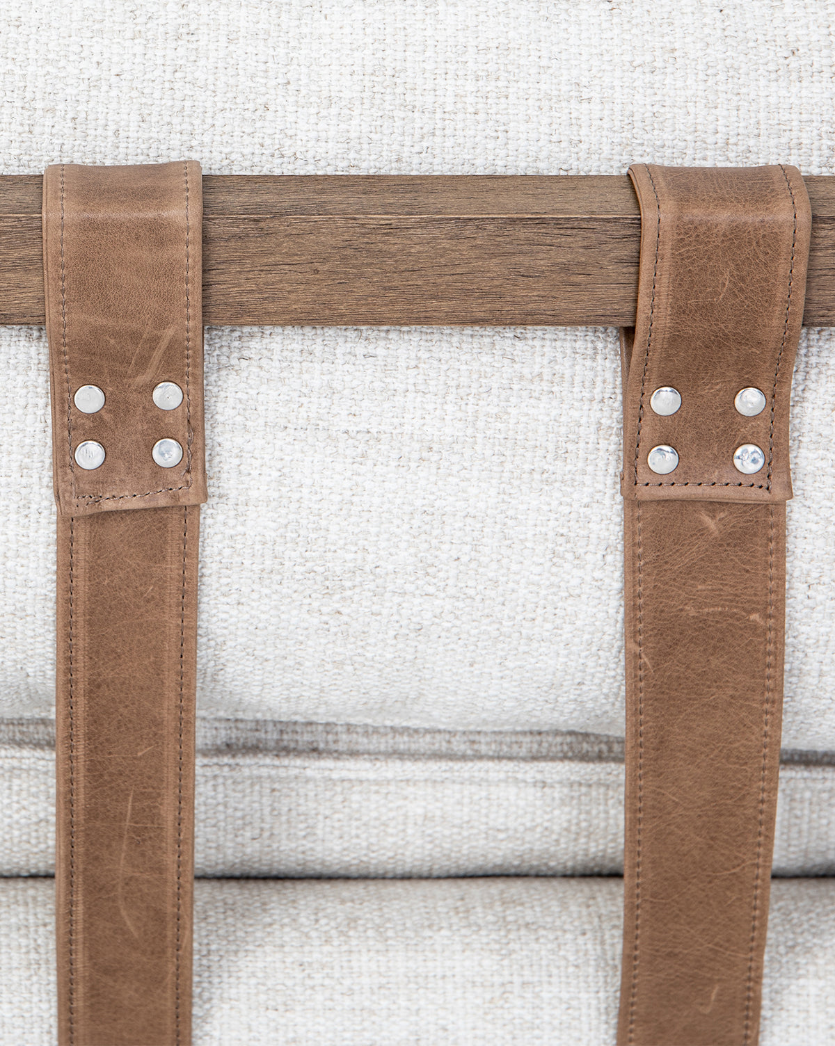 Close-up of taupe leather buckles with metal rivets on the Aberdeen Day Bed’s parawood frame, displayed against a textured light beige fabric background, by Vendixs
