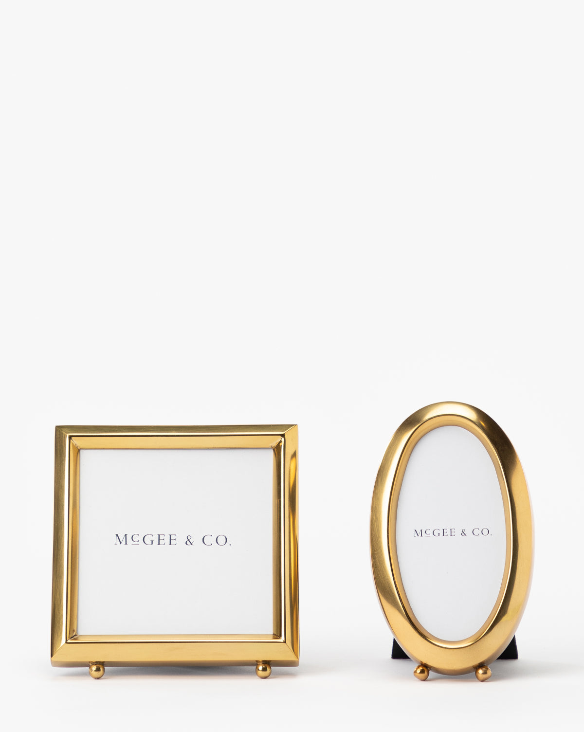 Two small Blanche Picture Frames, one square and one oval, feature an antique brass finish and white Vendixs inserts. These gold metal frames stand upright on a plain white background, adding vintage charm.