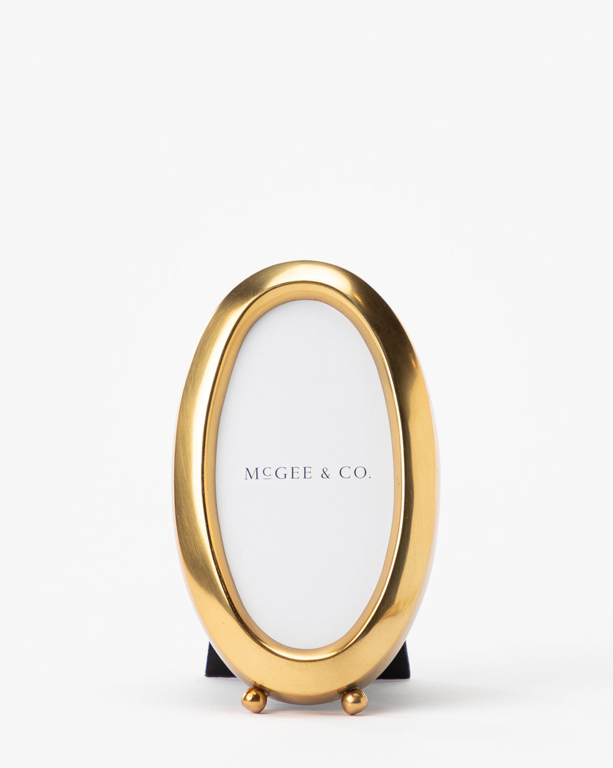 An oval Blanche Picture Frame with an antique brass, shiny finish stands upright against a white background, featuring Vendixs on the insert.