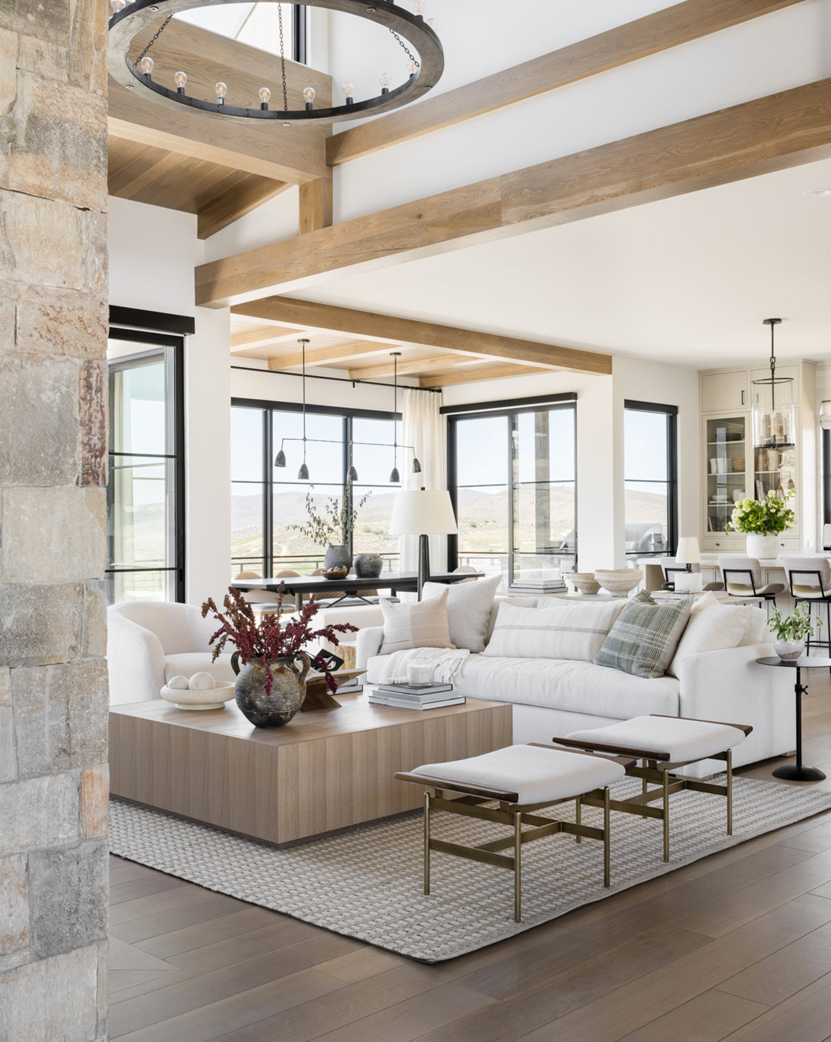 A modern living room features the Macy Upholstered Sofa (84-96), a large wooden coffee table, neutral decor, and floor-to-ceiling windows. Exposed beams and soft natural light create a cozy, elegant atmosphere by Vendixs
