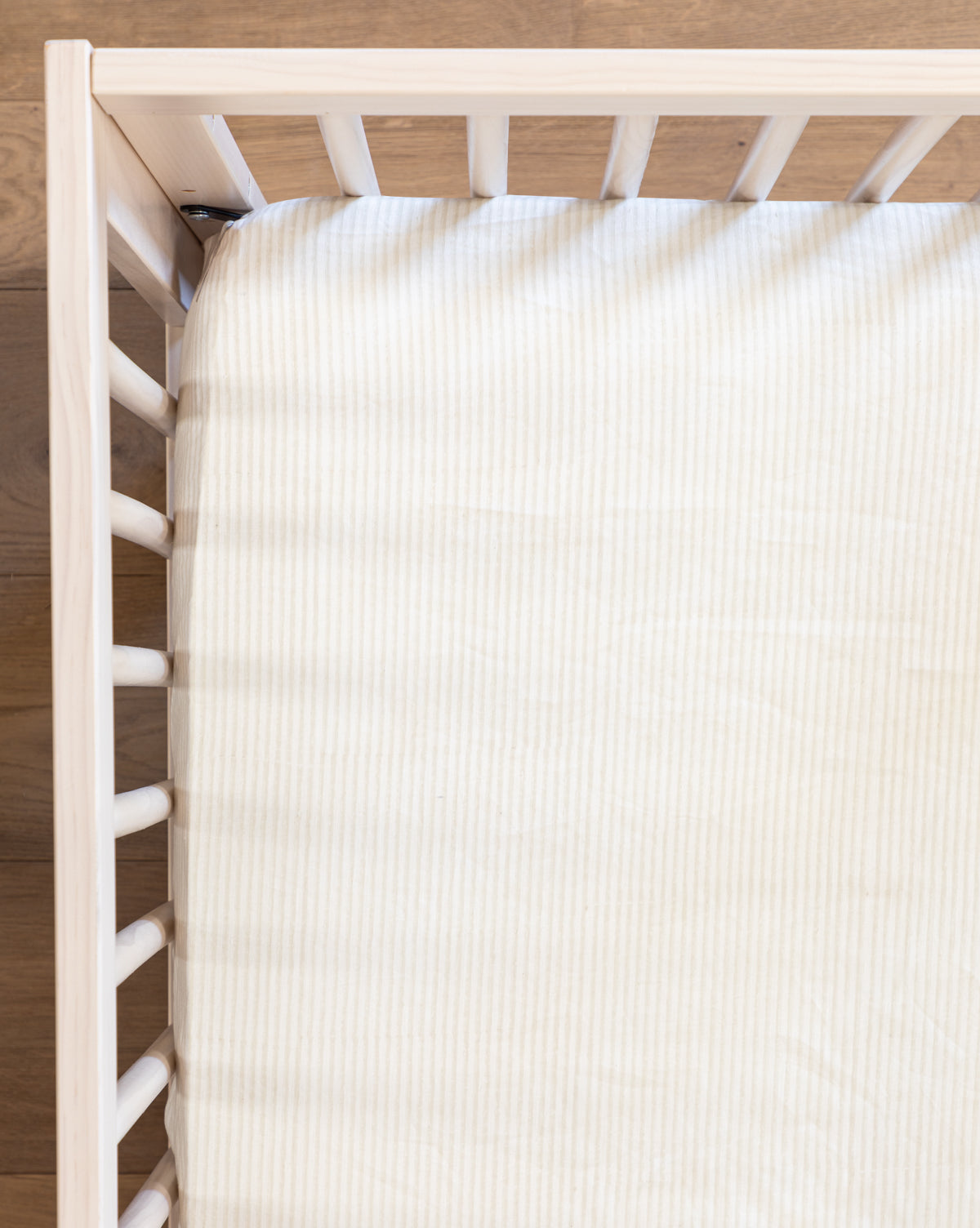 Top view of a white baby crib in a nursery, showcasing the Easton Crib Sheet with subtle stripes on the mattress, all placed on a wooden floor.