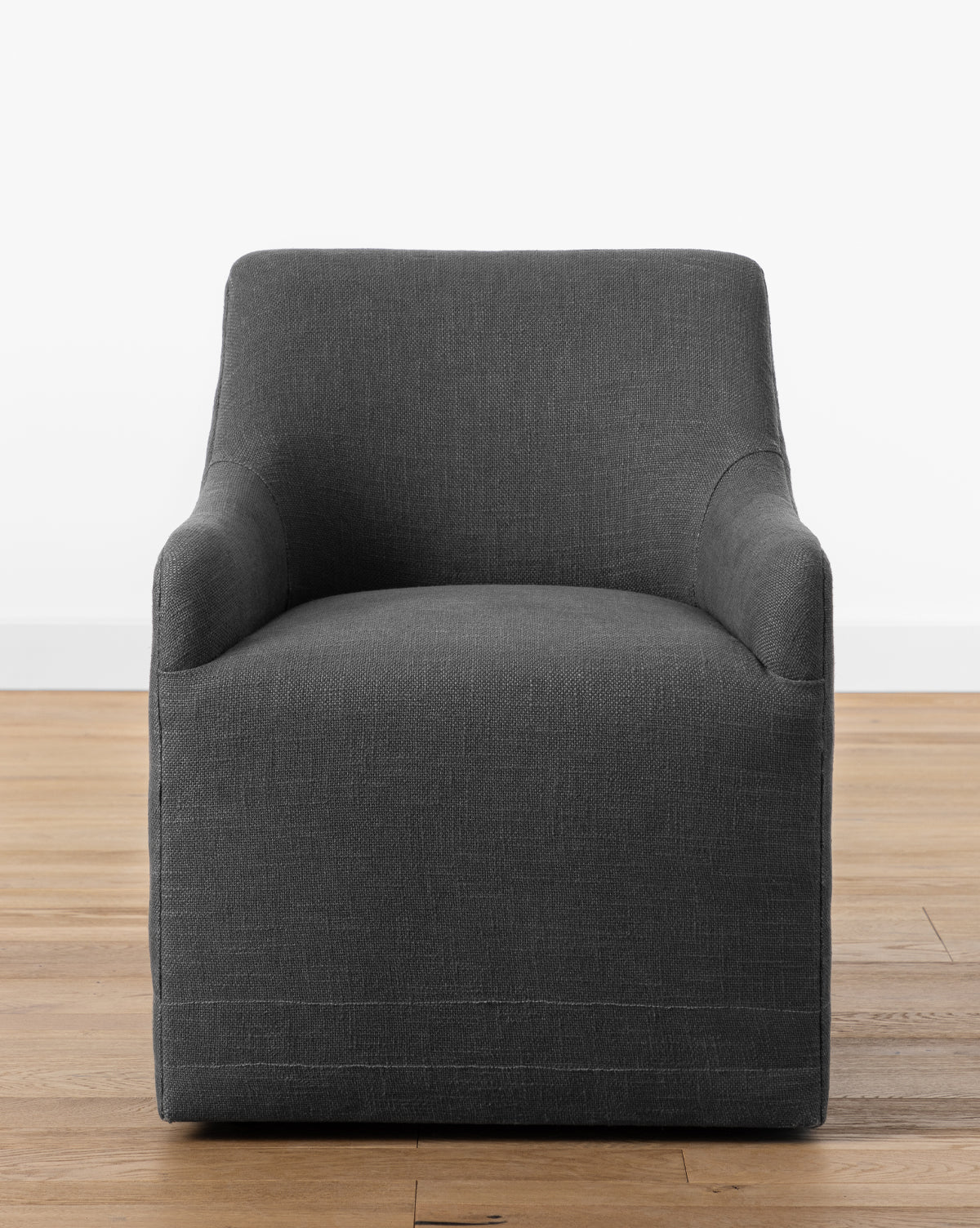 The Elton Office Chair features a modern boxy design with dark gray linen-blend upholstery, slightly rounded arms, and adds office elegance when placed on a light wooden floor against a plain white wall, by Vendixs