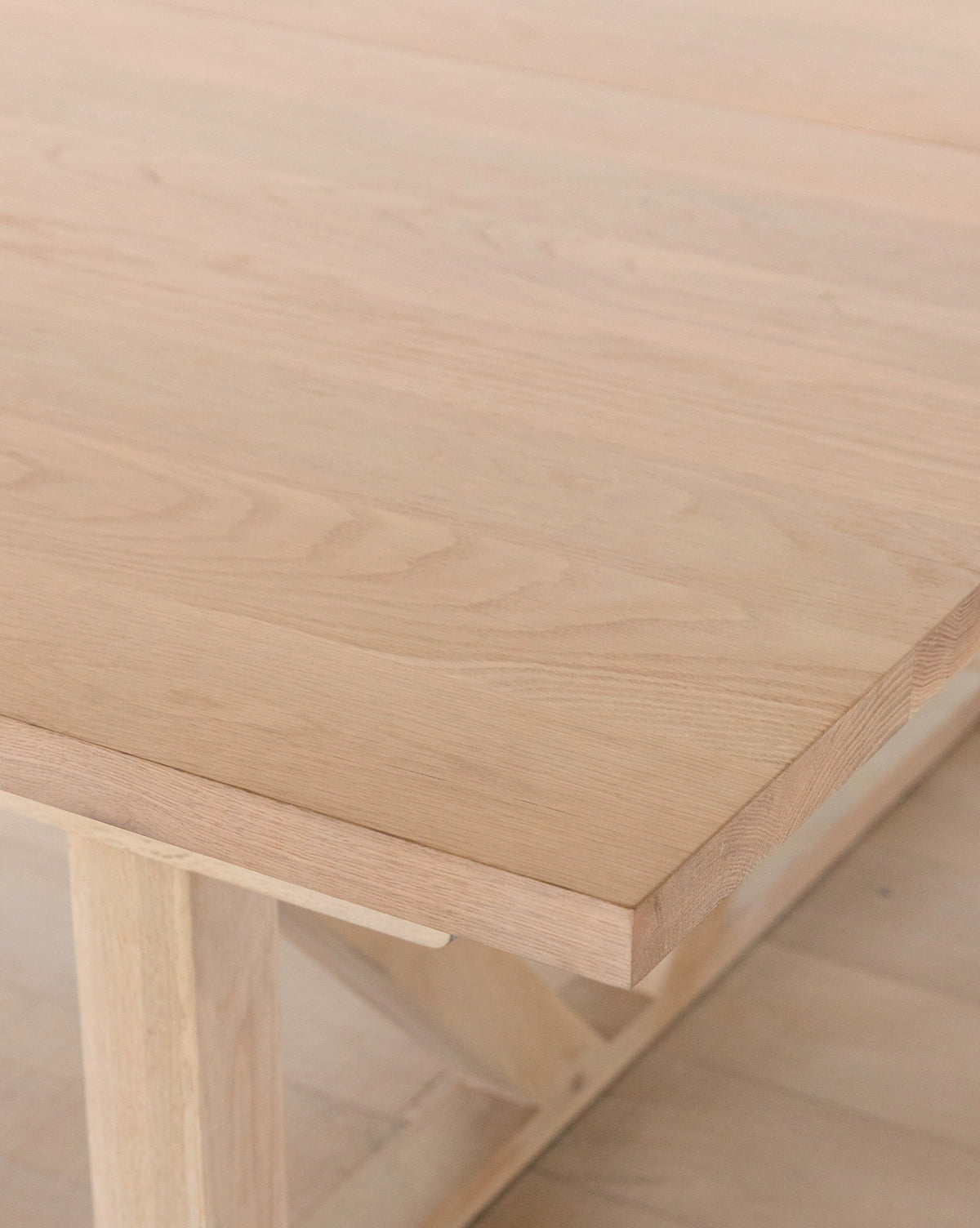 A close-up of the Emory Extension Dining Table shows its solid oak construction, smooth natural finish, and visible wood grain. The tables architectural base and part of the floor are also partially visible by McGee & Co.