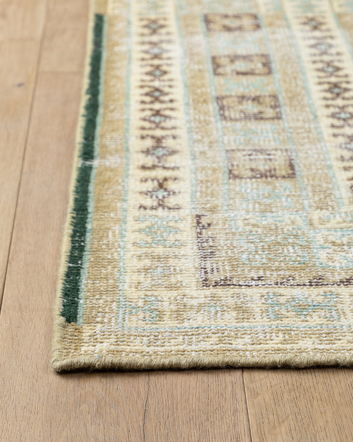 A close-up of the Evangeline Hand-Knotted Wool Rug’s corner on a light wooden floor, showcasing its durable wool texture and geometric border design, by Vendixs