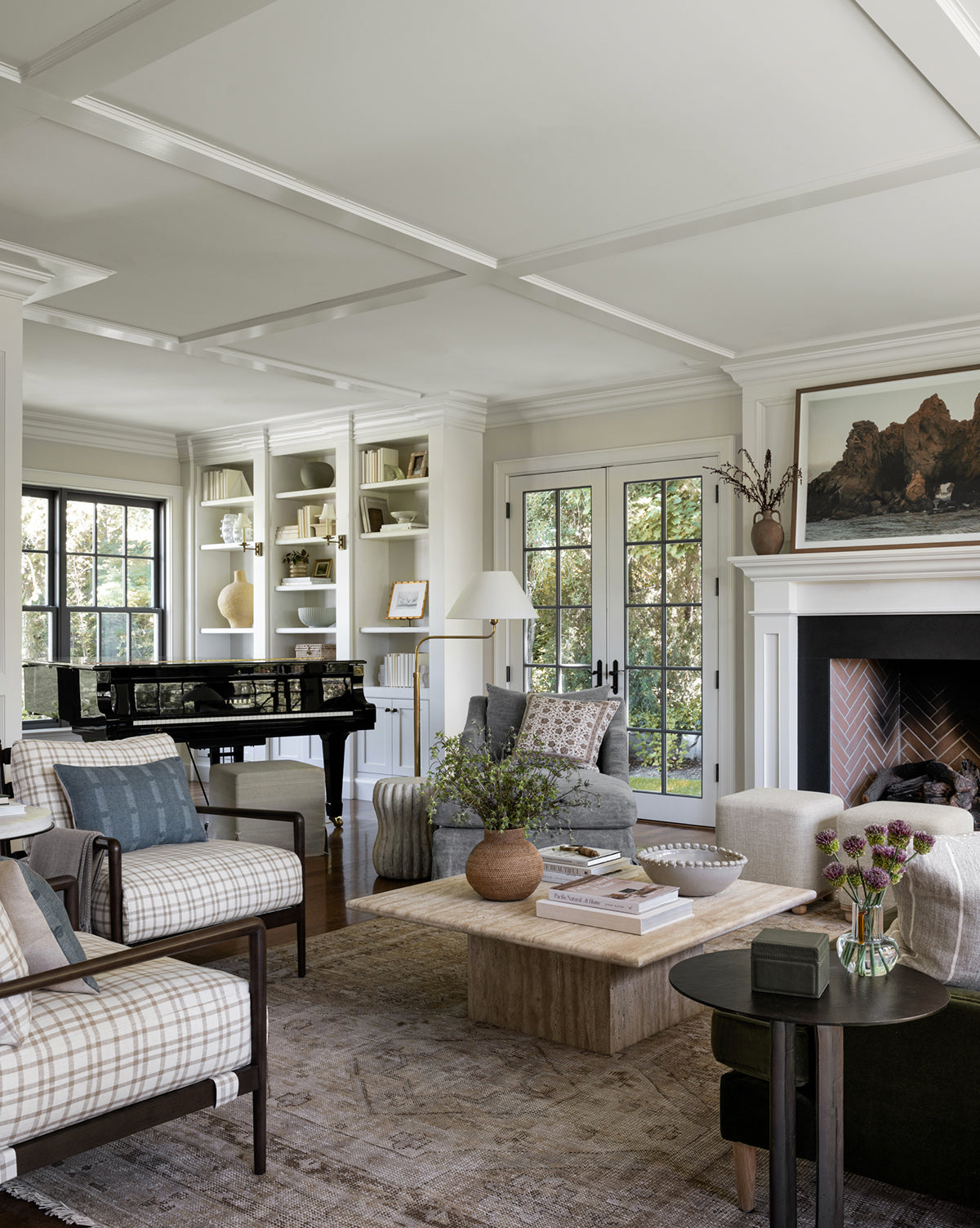 A bright, elegant living room with large windows, a black grand piano, built-in white shelves, a cozy armchair, fireplace with art above, and neutral furniture arranged on the Charlot Hand-Knotted Rug, by Vendixs