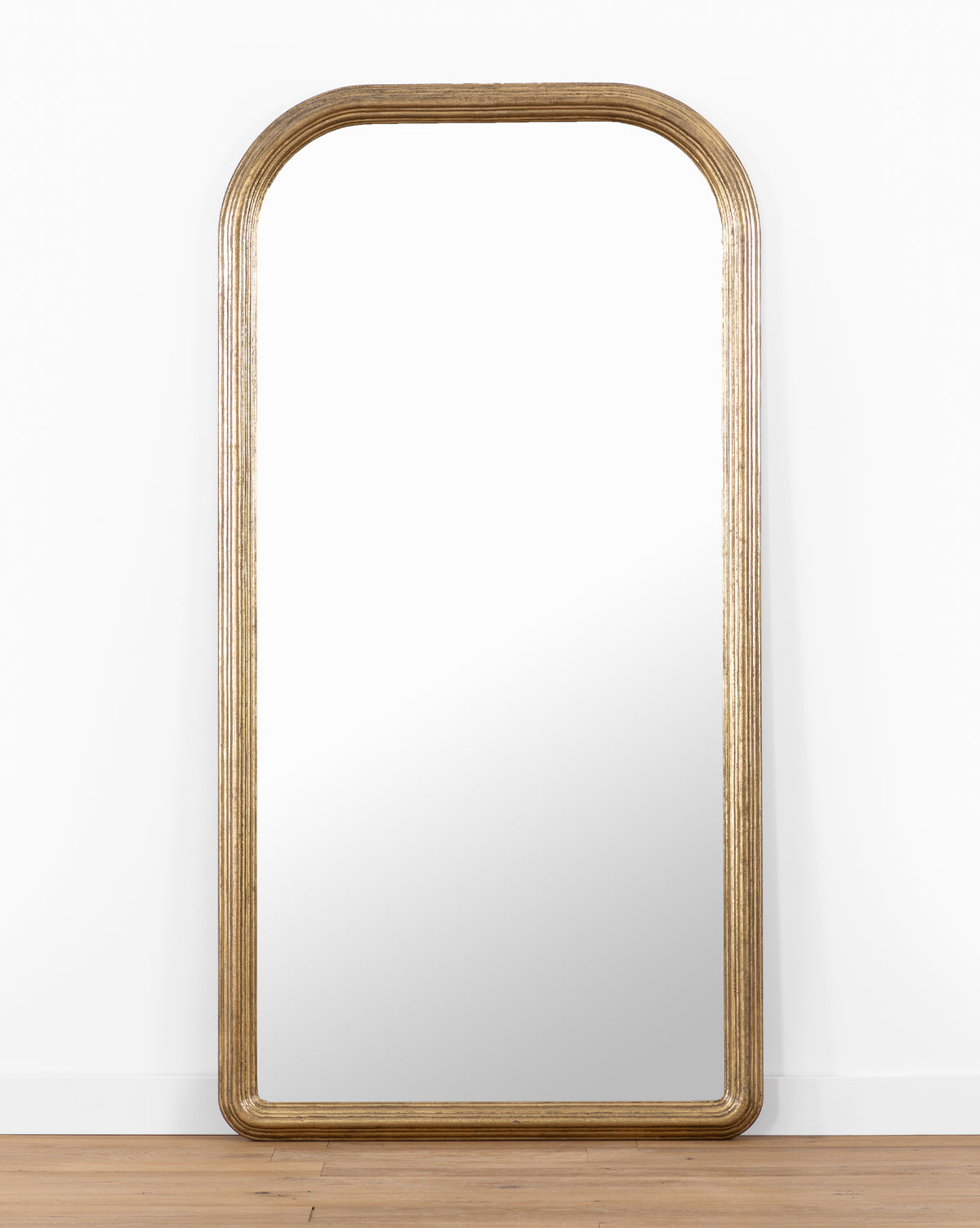 The Giada Floor Mirror showcases a large rectangular design with a rounded top and an elegant gold-toned frame, making it the ideal accent for traditional interiors, by McGee & Co.