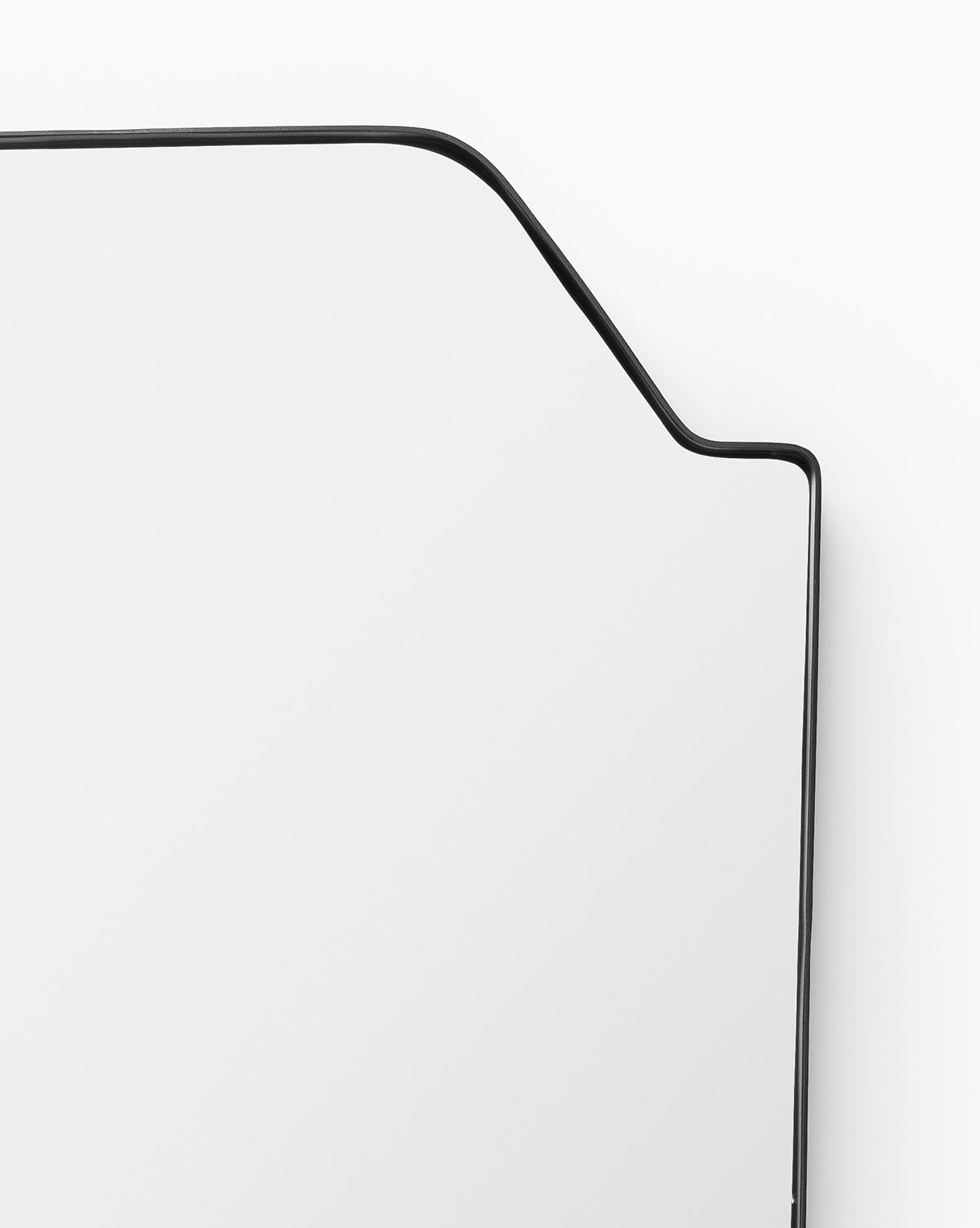 A close-up of the Giles Wall Mirror highlights its thin, matte black asymmetric frame bending at an angle, creating a striking modern geometric shape against a plain white background, by Vendixs