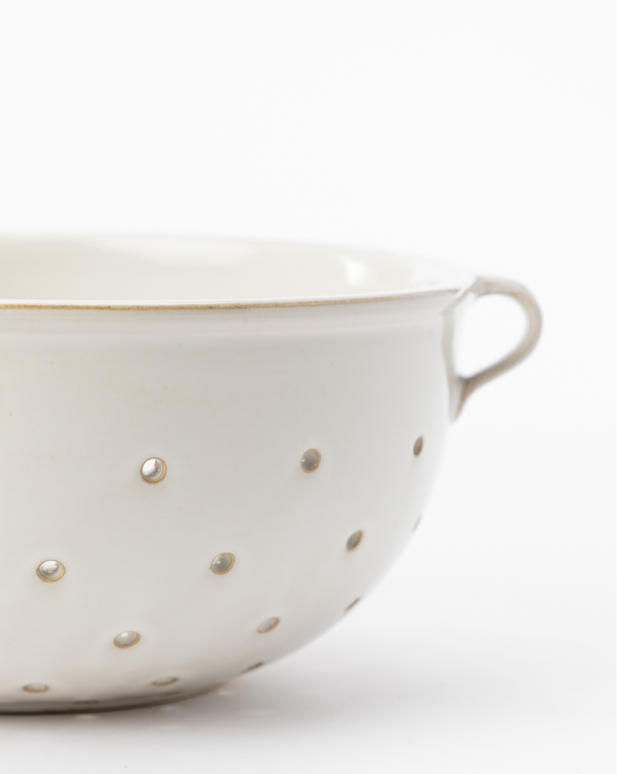 A close-up of a white ceramic Glazed Colander featuring small holes and a handle, ideal for serveware or kitchen decor, shown against a plain white background, by Vendixs