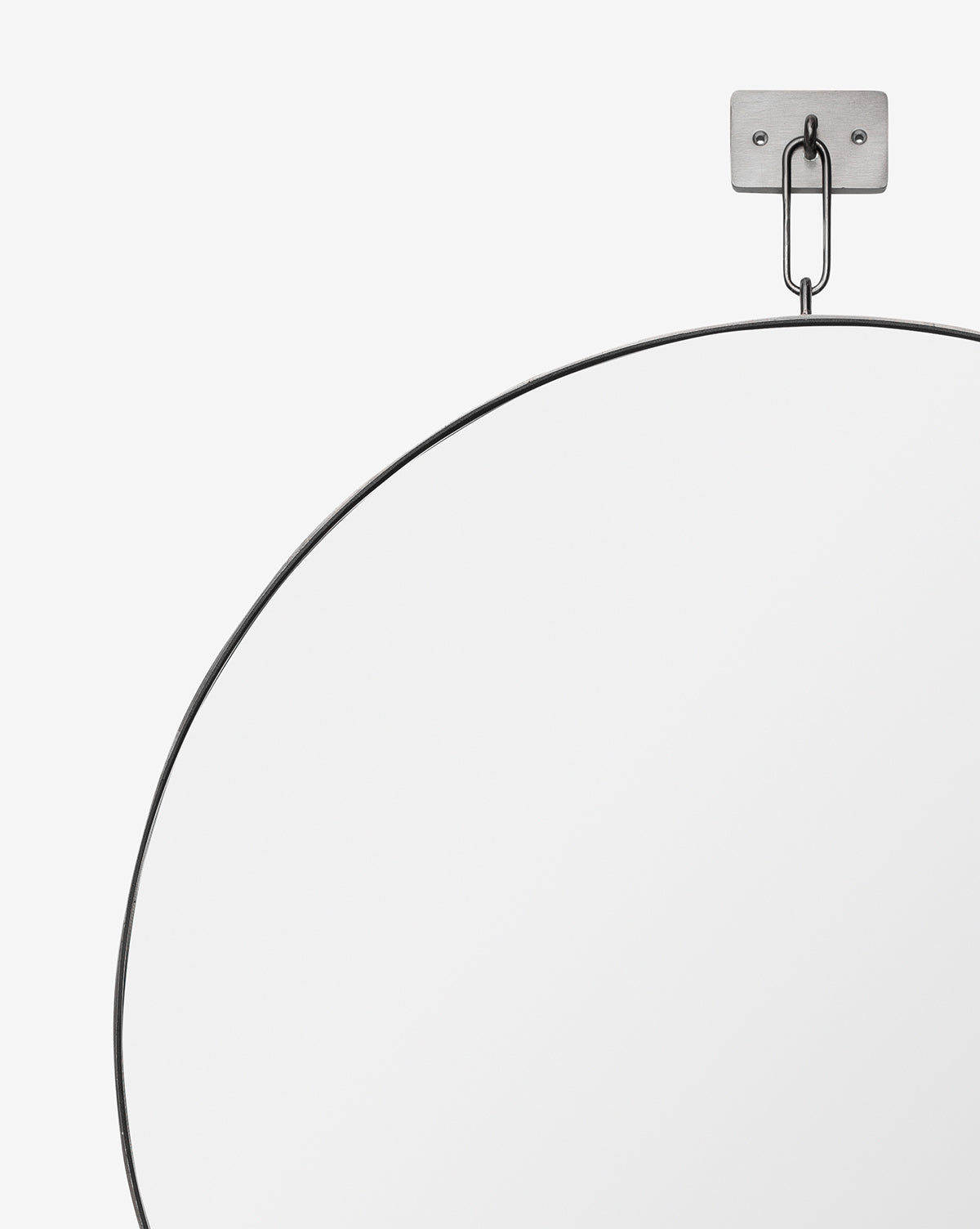 The Haven Wall Mirror features a modern thin black frame and hangs from a rectangular stainless steel wall mount and chain against a plain white background, with only the upper portion of the mirror visible, by Vendixs