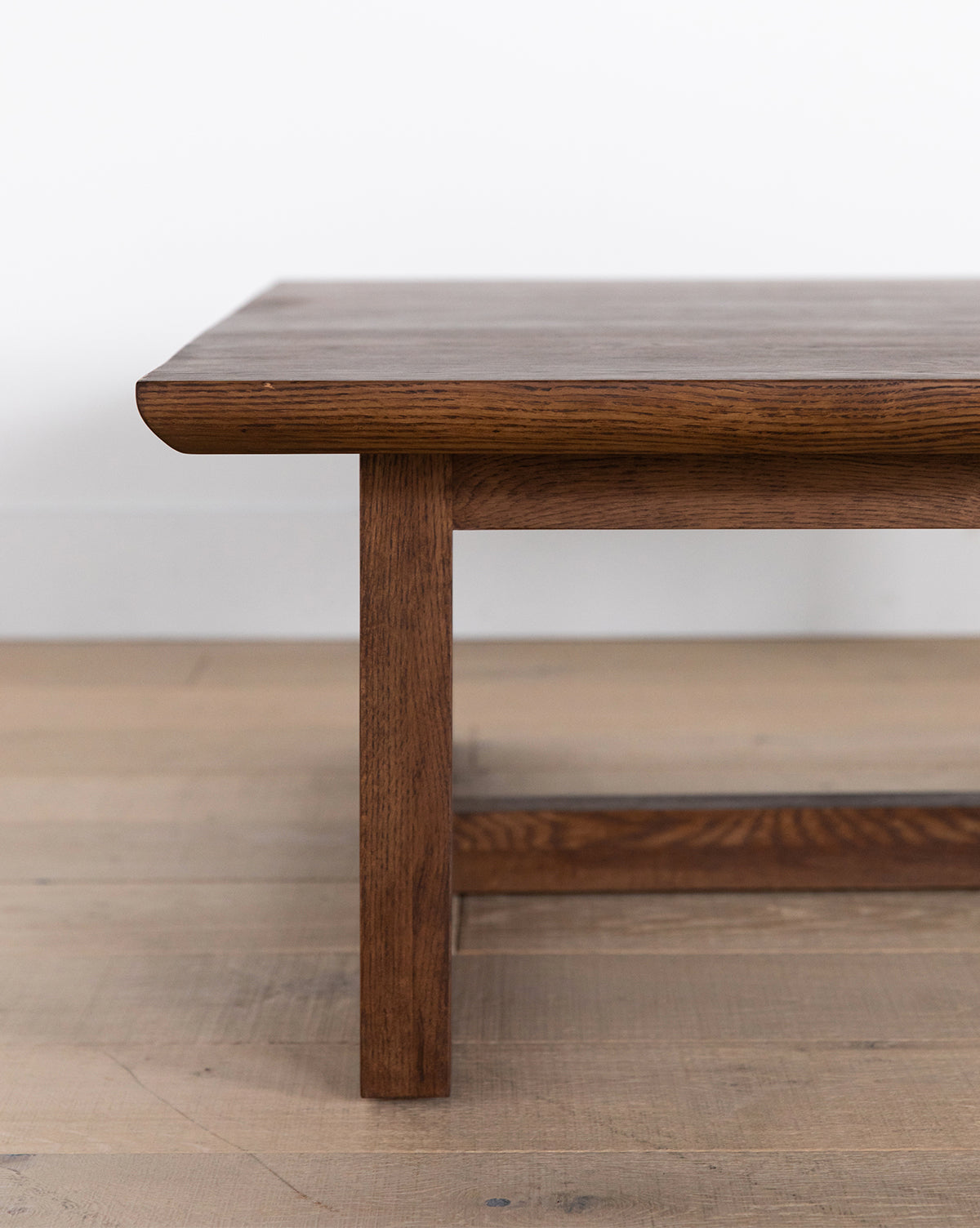 A close-up of the Herrin Coffee Table shows its smooth rectangular top and sturdy legs, set on a light wood floor with a white wall in the background, by Vendixs