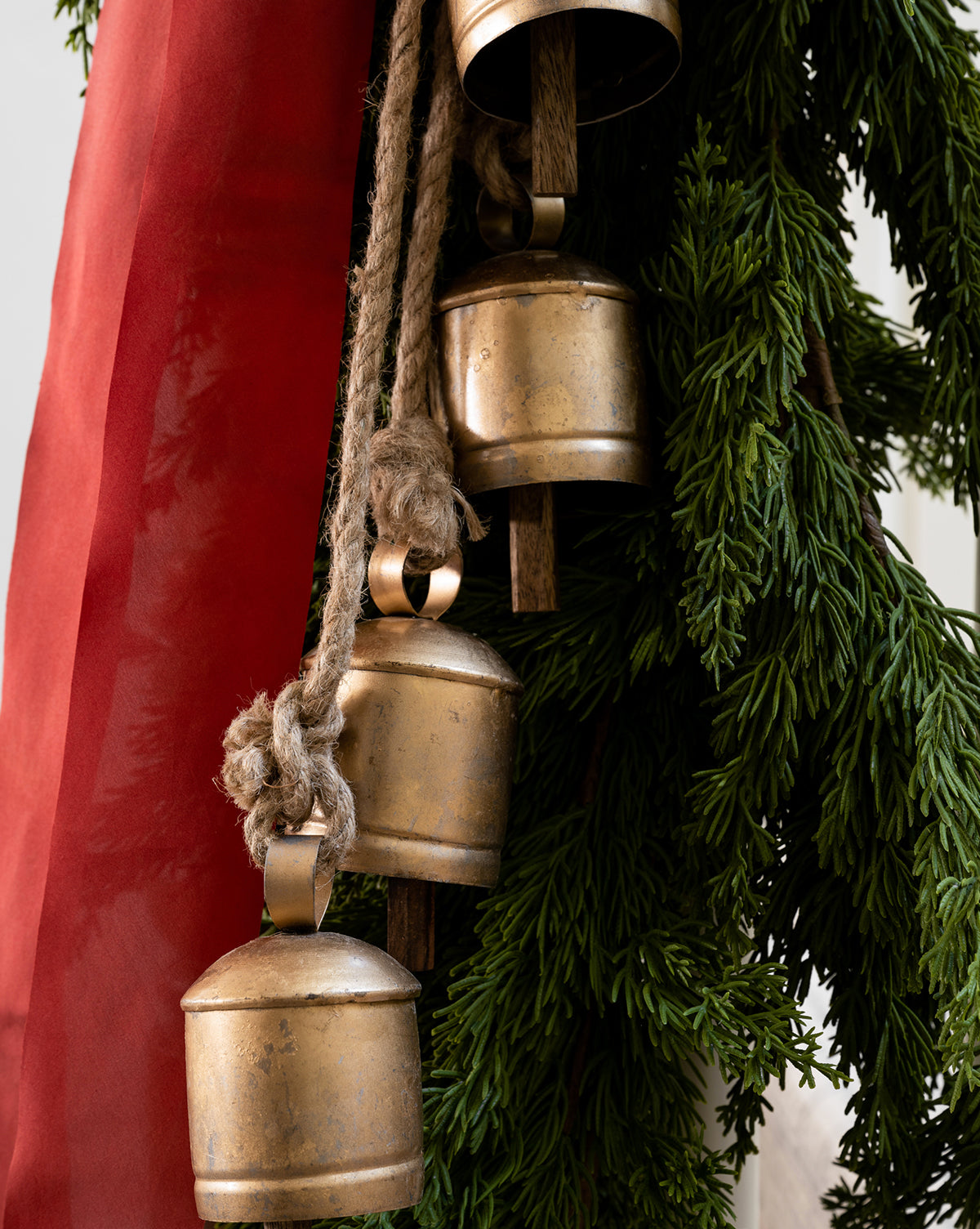 Close-up of three Hanging Iron Bells with a gold finish, suspended by thick rope beside green fir branches and a red ribbon, adding festive charm and rustic holiday décor, by Vendixs