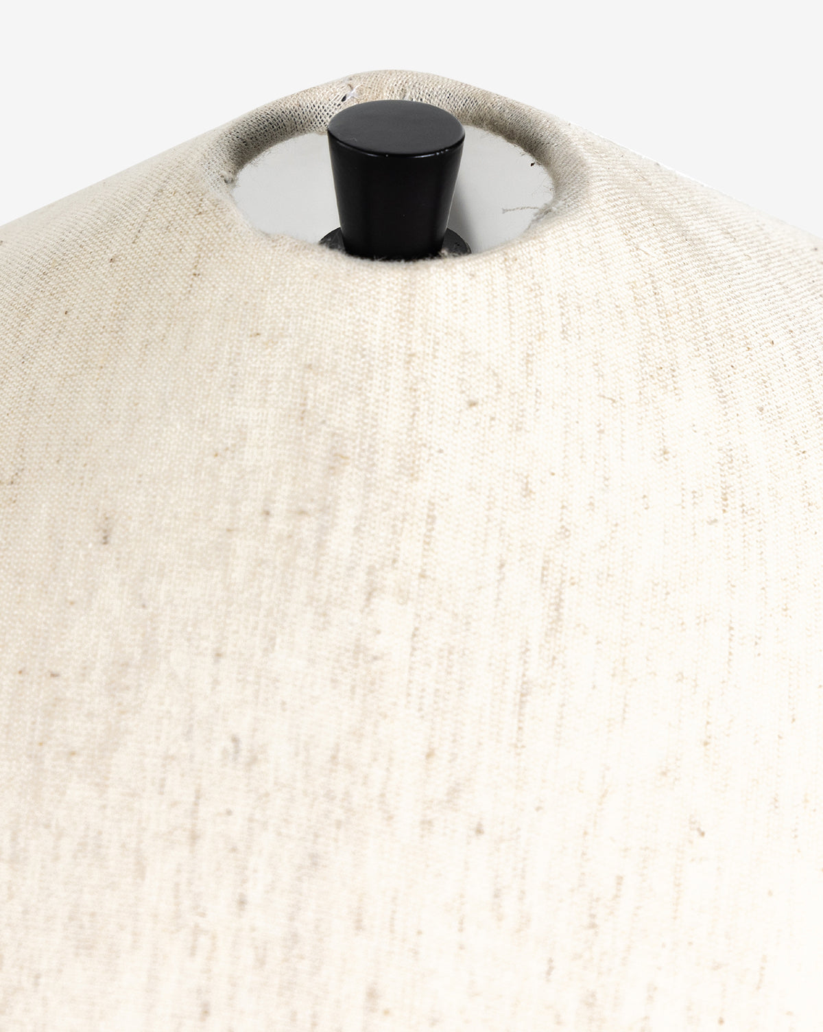 Close-up of the top part of the Innes Tapered Table Lamp’s light beige fabric shade with a black finial and silver hardware at the center, complementing décor such as a basket weave mirror, by Vendixs