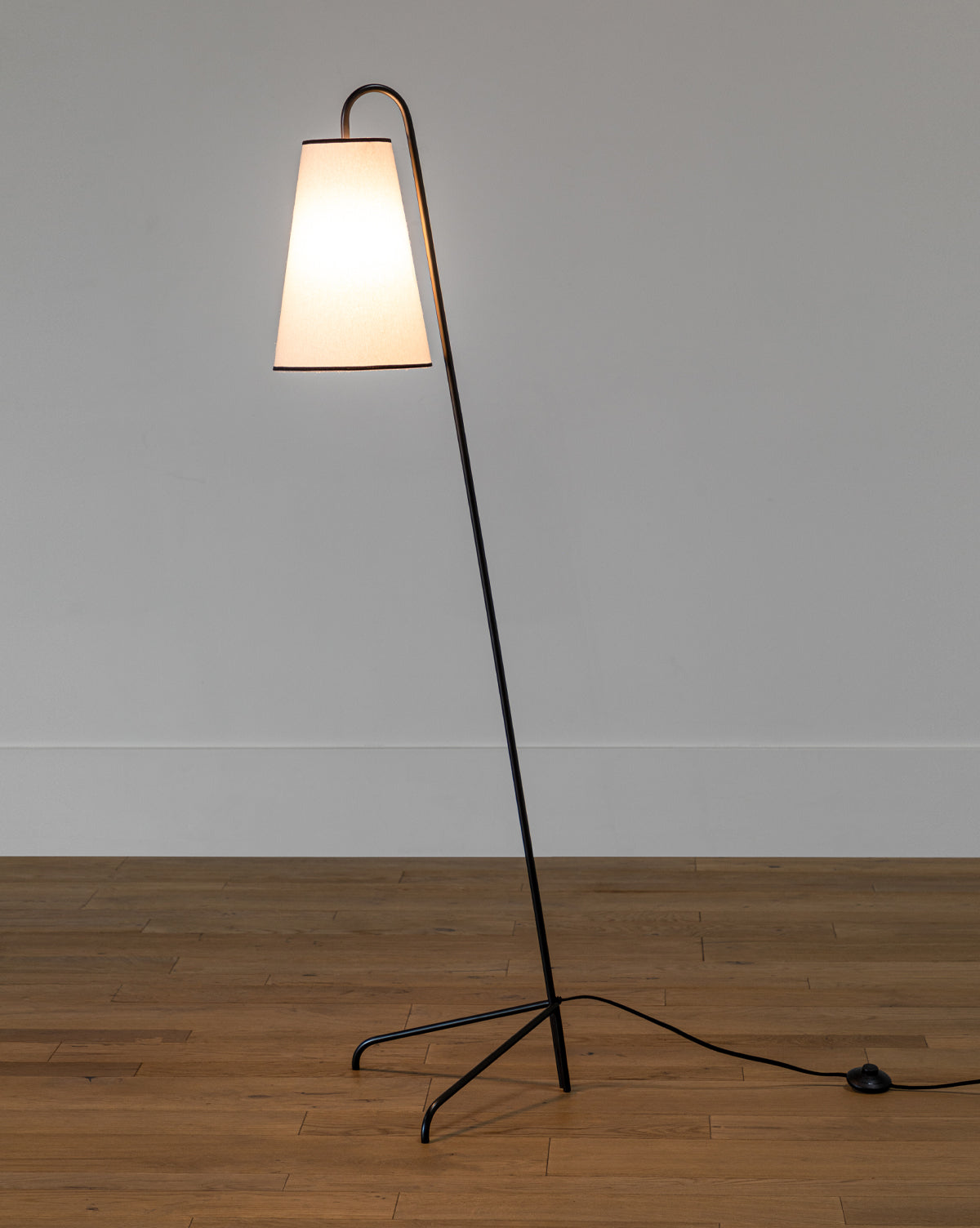 The Jonas Floor Lamp has a slim black metal frame, angled stem, tripod base, and white linen shade, creating an elegant look for any room, by McGee & Co.