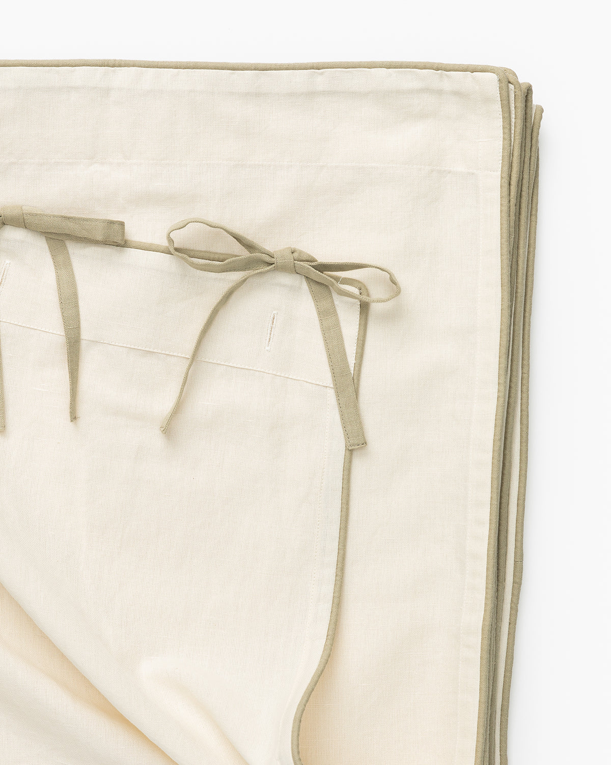The Lillian Linen Shower Curtain features off-white linen accented with light khaki-green borders and tie closures, reminiscent of neatly folded, elegant napkins, shown against a clean white background.