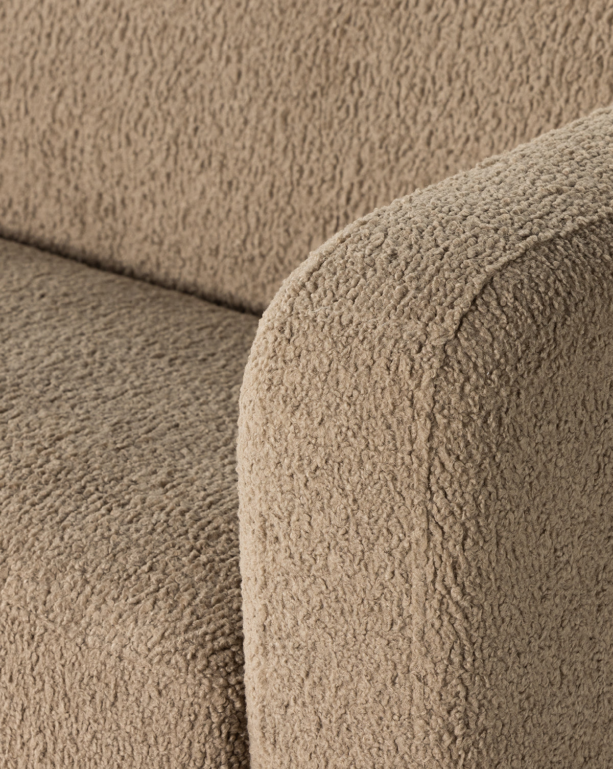 Close-up of the arm and seat of the Quill Sofa 84 by Four Hands, featuring beige faux shearling upholstery thats soft, plush, and slightly curly, evoking vintage sofa designs. Vendixs