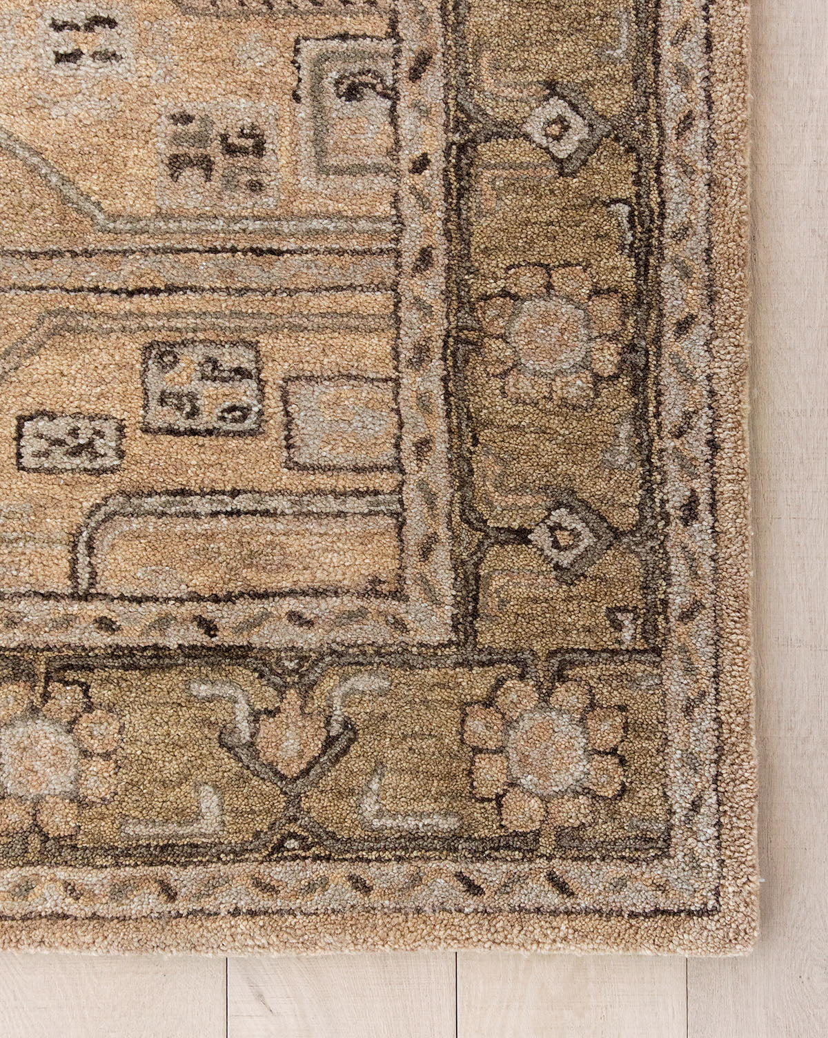 Corner of the Ellington Fawn Hand-Tufted Wool Rug, featuring beige and tan tones, intricate geometric and floral designs, a stylized floral border, and abstract rectangular motifs, shown on a light wood floor, by Vendixs