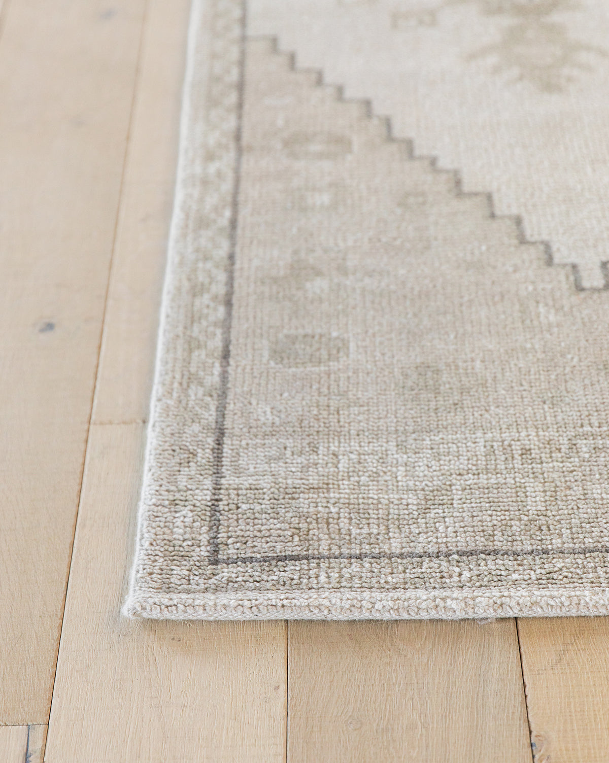 A close-up of the Pembroke Hand-Knotted Wool Rug on light wooden flooring. This beige and light gray rug features subtle geometric patterns and a thin border, bringing vintage-inspired charm to any room, by Vendixs