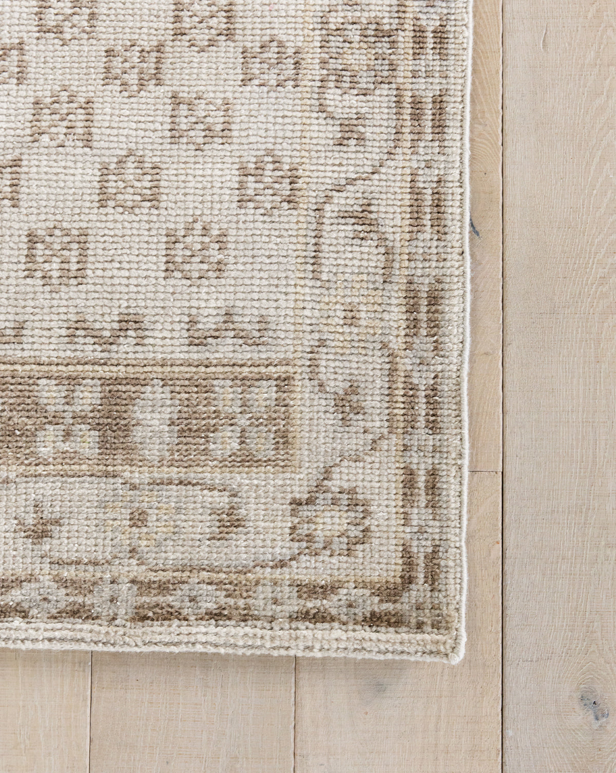 A close-up of the Anya Neutral Hand-Knotted Wool Rug on a light wood floor, showcasing its geometric and floral patterns, woven texture, and detailed edging, by Vendixs