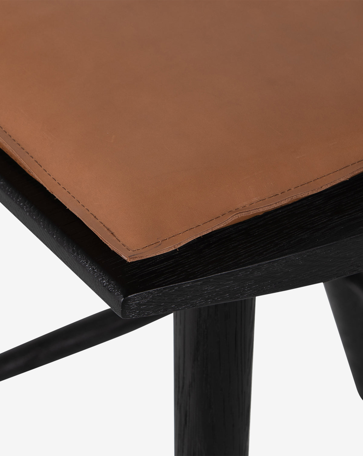 Close-up of the Madison Stools corner, featuring a brown leather seat with visible stitching and a black wooden frame—showcasing the textured materials ideal for a cushioned Windsor-style stool, by Vendixs