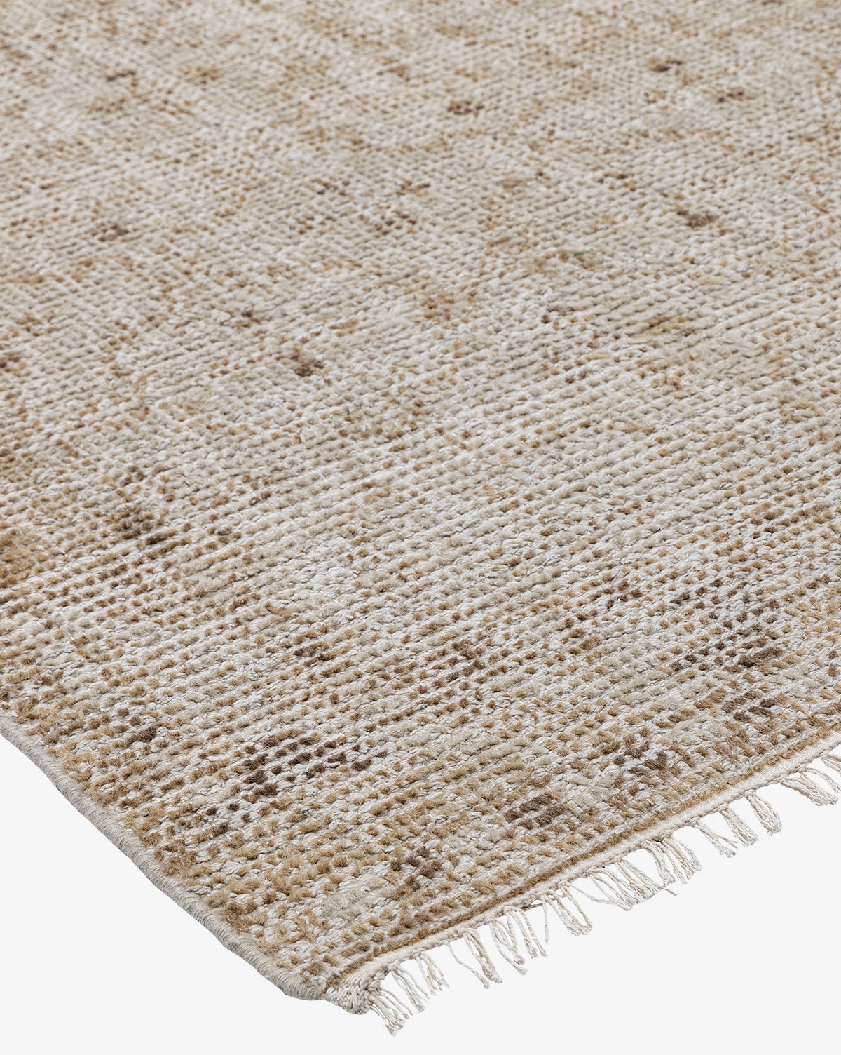 A close-up of the Mali Hand-Knotted Rug showcases its neutral tones, subtle geometric patterns, and small fringe tassels along one edge, featuring a textured, slightly rustic look, by Vendixs