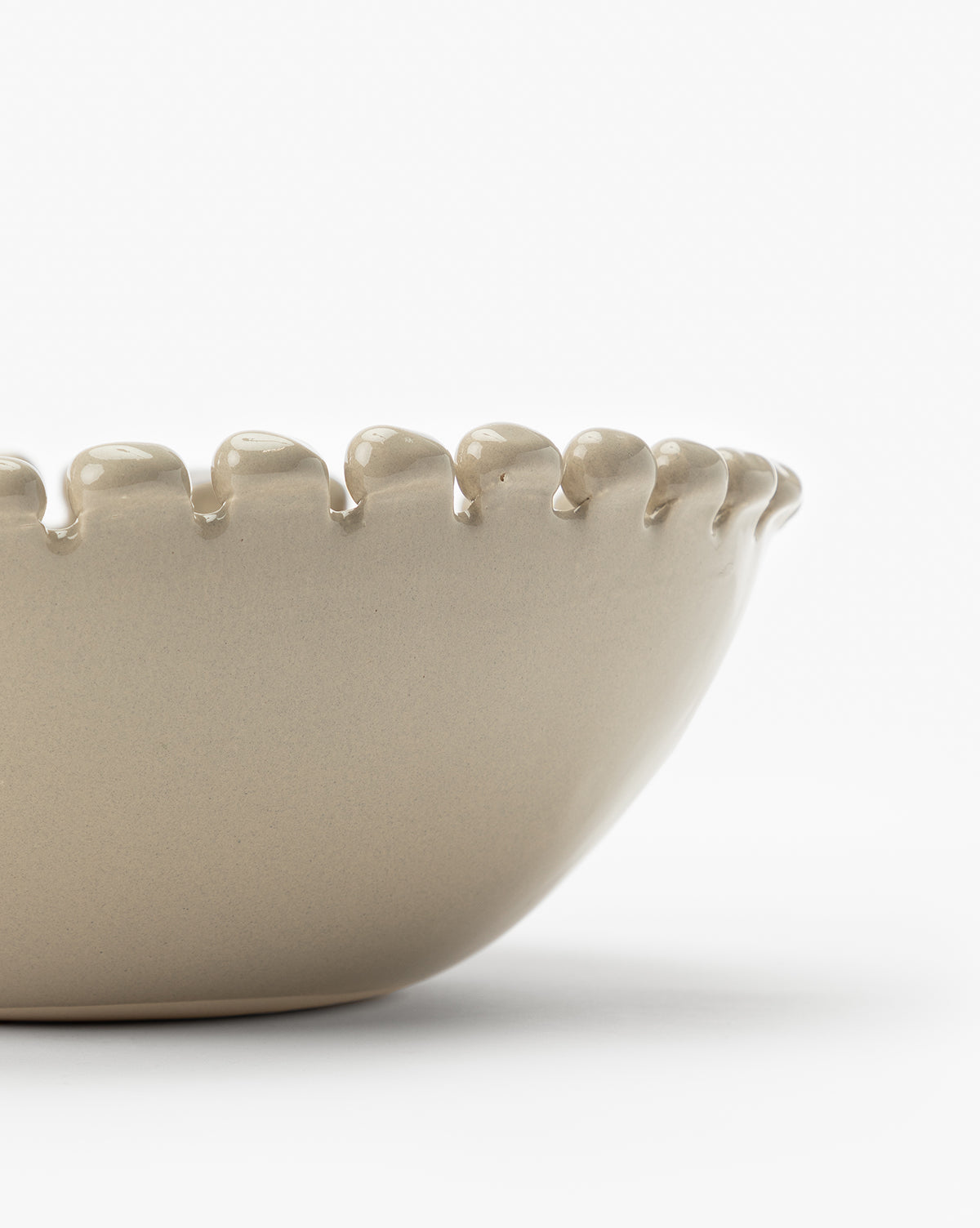 A close-up of the Malibu Bowl, a beige ceramic piece with a scalloped, rounded rim, is shown against a white background. Only part of this unique kitchen décor item is visible in the image, by Vendixs