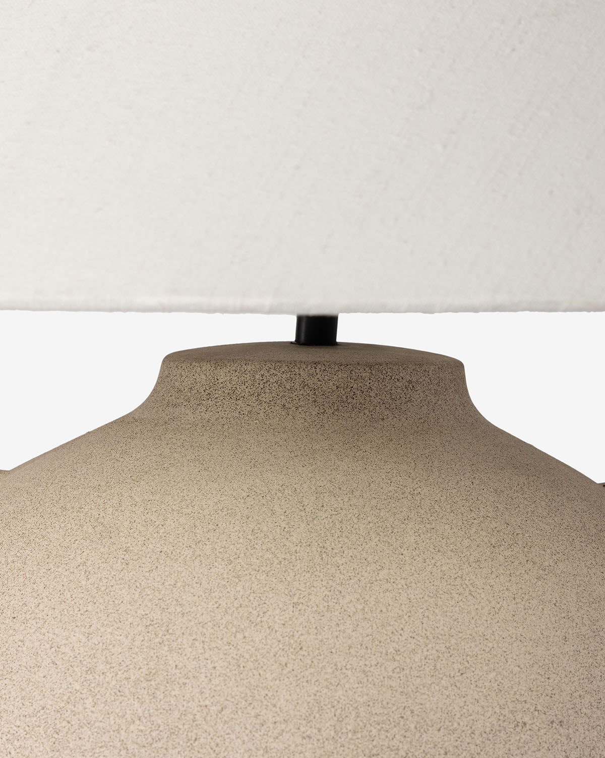 Close-up of the top portion of the sand-colored Mays Table Lamp base with a white fabric lampshade above it, set against a plain background by Vendixs