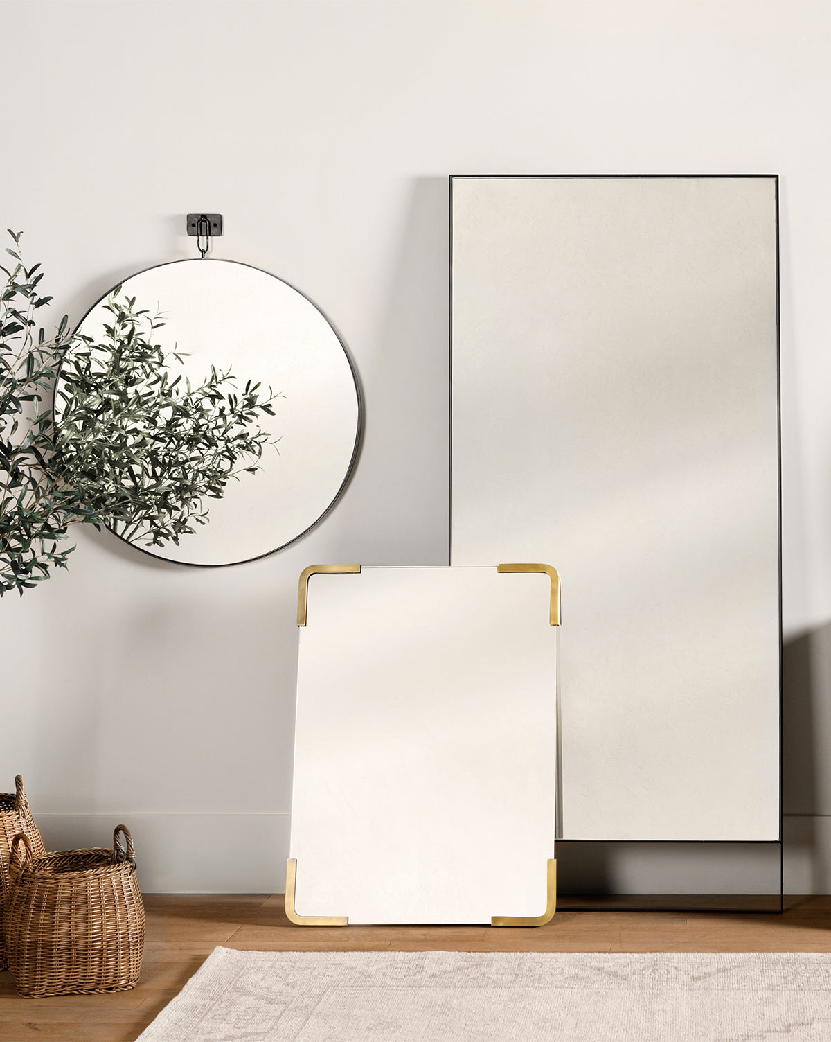 A minimalist room features the Mare Mirror, a round frameless mirror, and a small rectangular mirror with gold corners. A woven basket and a plant bring warmth to the neutral, modern decor, by Vendixs
