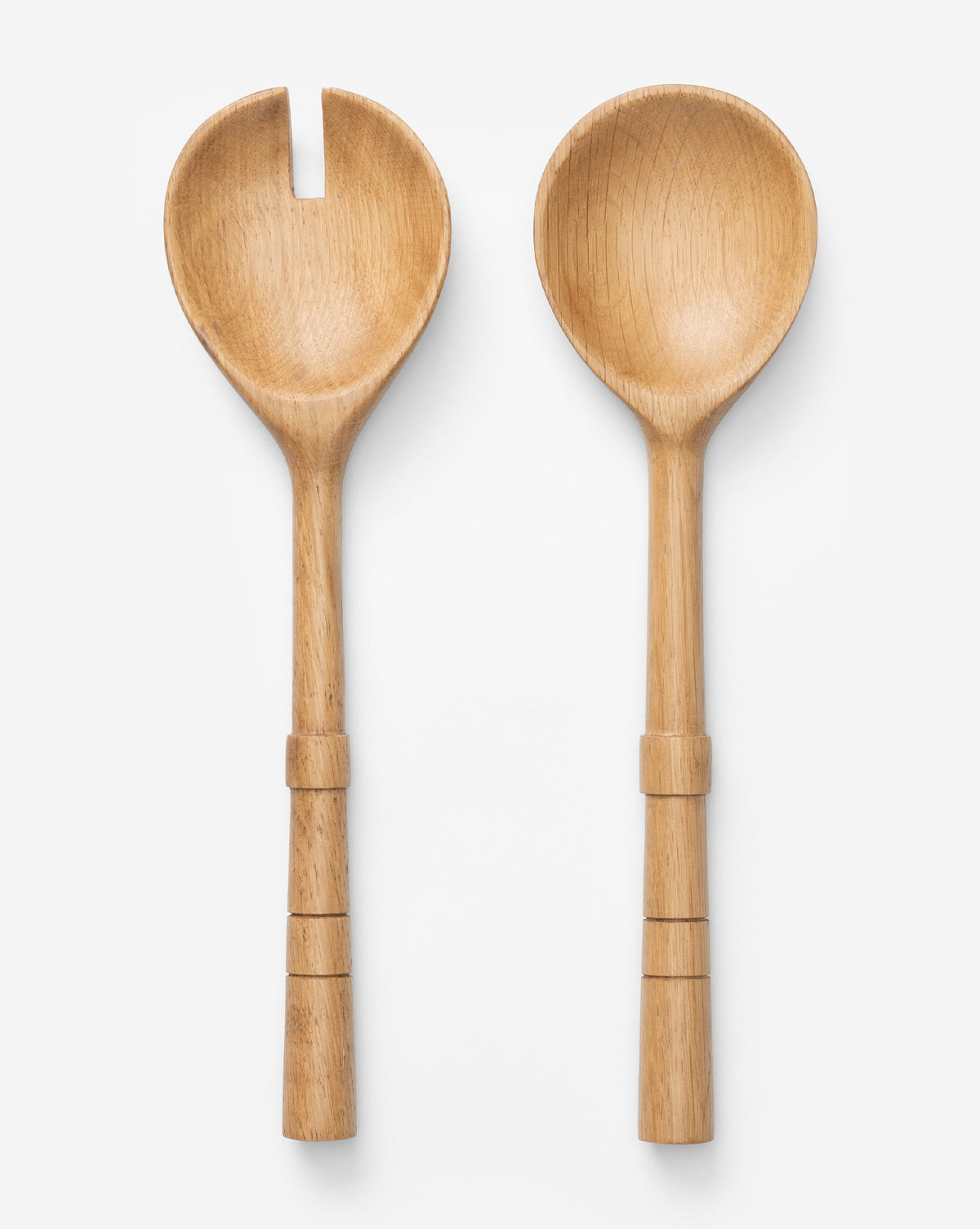 The Notched Oak Wood Salad Servers rest on a white background—one is a fork, the other a spoon. Both have rounded, notched handles with carved rings, creating an elegant and organic serving set by McGee & Co.