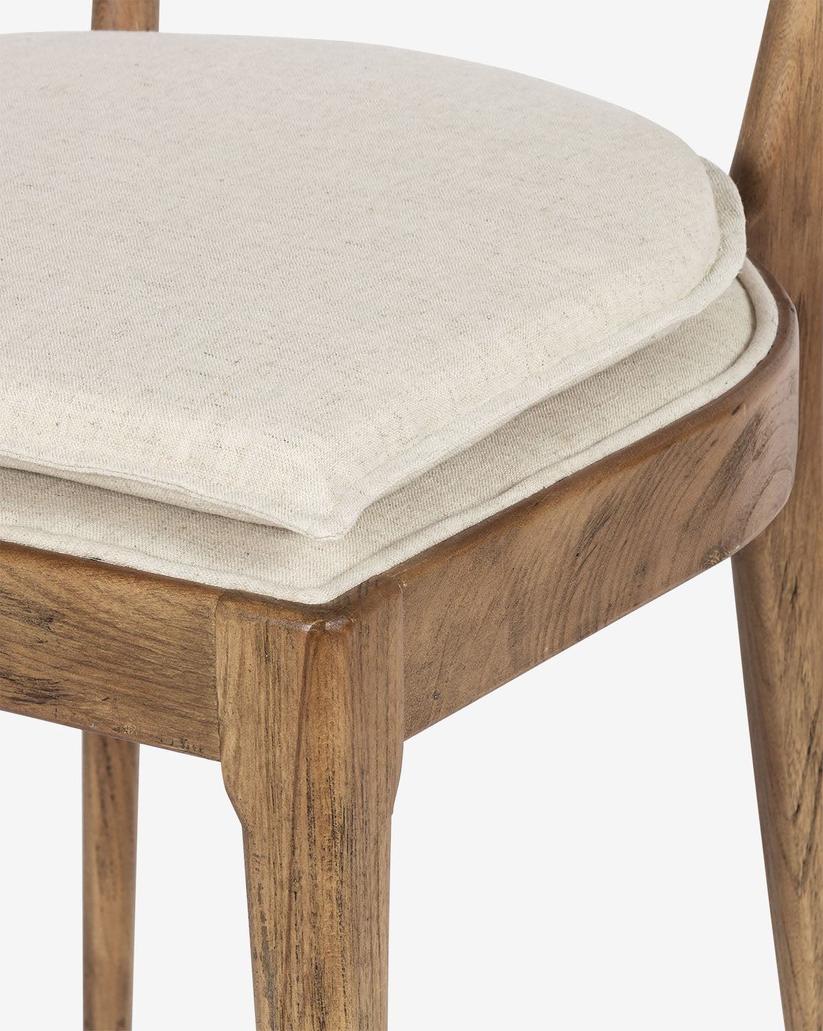 Close-up of the Odelle Dining Chair, showcasing its modern wooden frame, light beige upholstered seat with extra padding, and detailed fabric texture alongside the natural wood grain, by McGee & Co.