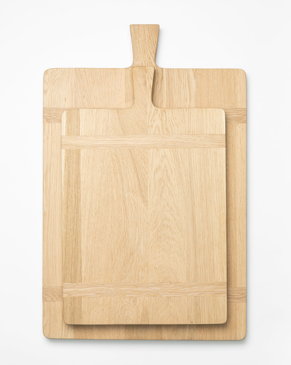 Two Rectangle Bread Boards with handles, made from oak and walnut, are stacked on a white surface. The smaller board sits on the larger, both showcasing their natural finish and unique wood grain, by Vendixs