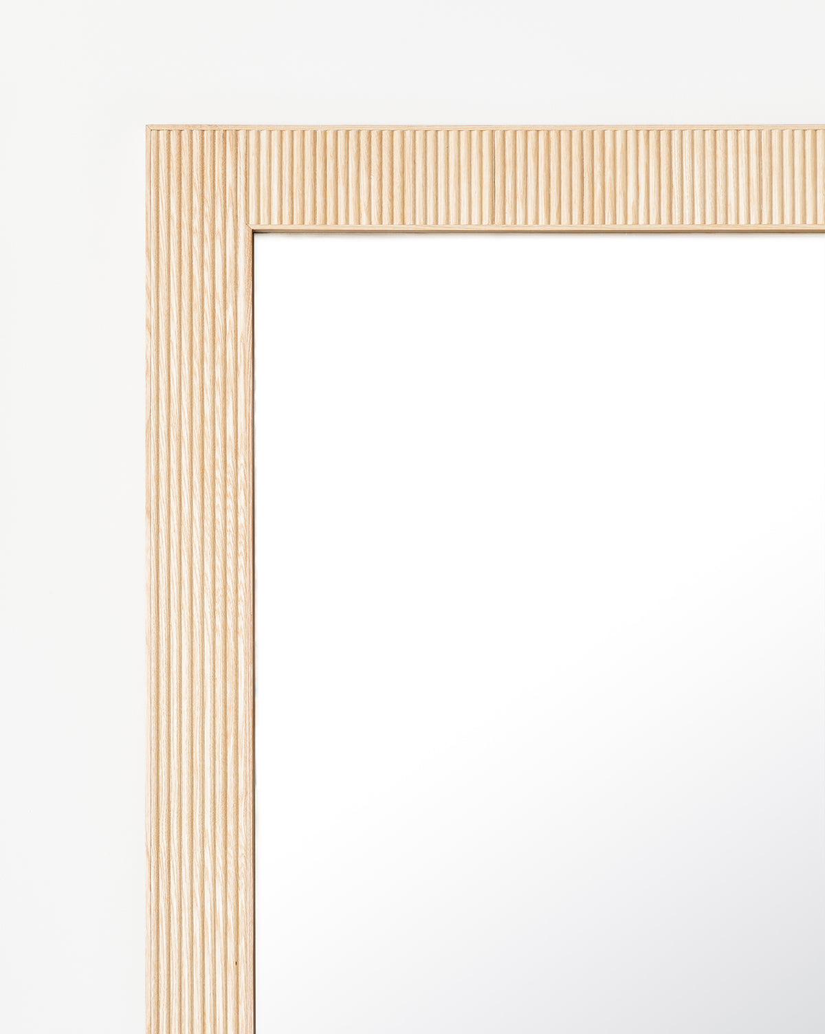 Close-up of the top left corner of the Rowan Floor Mirror, highlighting its ribbed oak frame with vertical texture set against a plain white background, by Vendixs