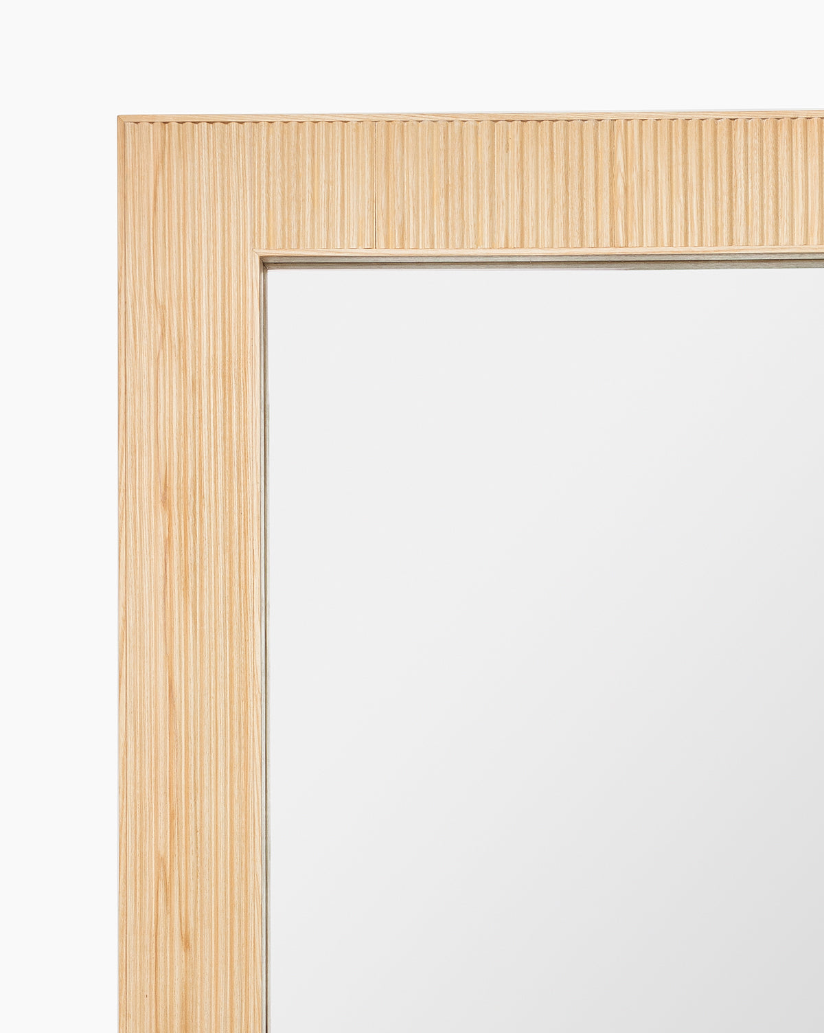 Close-up of the Rowan Wall Mirror’s top left corner, highlighting its ribbed ash wood frame with vertical grooves, set against a white background, by Vendixs