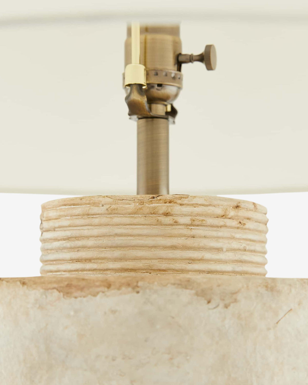 Close-up of the Samala Lamp, featuring a textured stone-like base with horizontal grooves for a vintage look, topped with a brass socket and partially shaded by a white lampshade by Vendixs