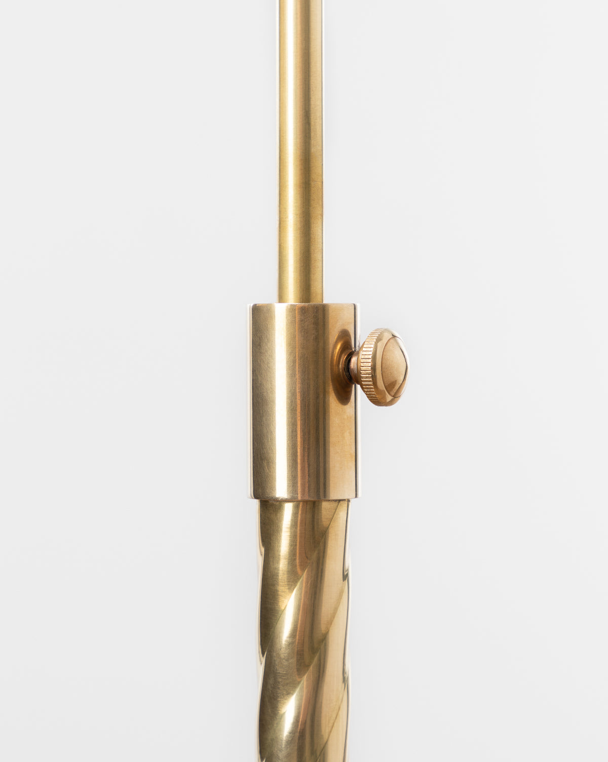 Close-up of the Saylor Floor Lamp’s brass adjustable rod with a knurled tightening knob and twisted lower section—an elegant detail—set against a plain white background, by Vendixs