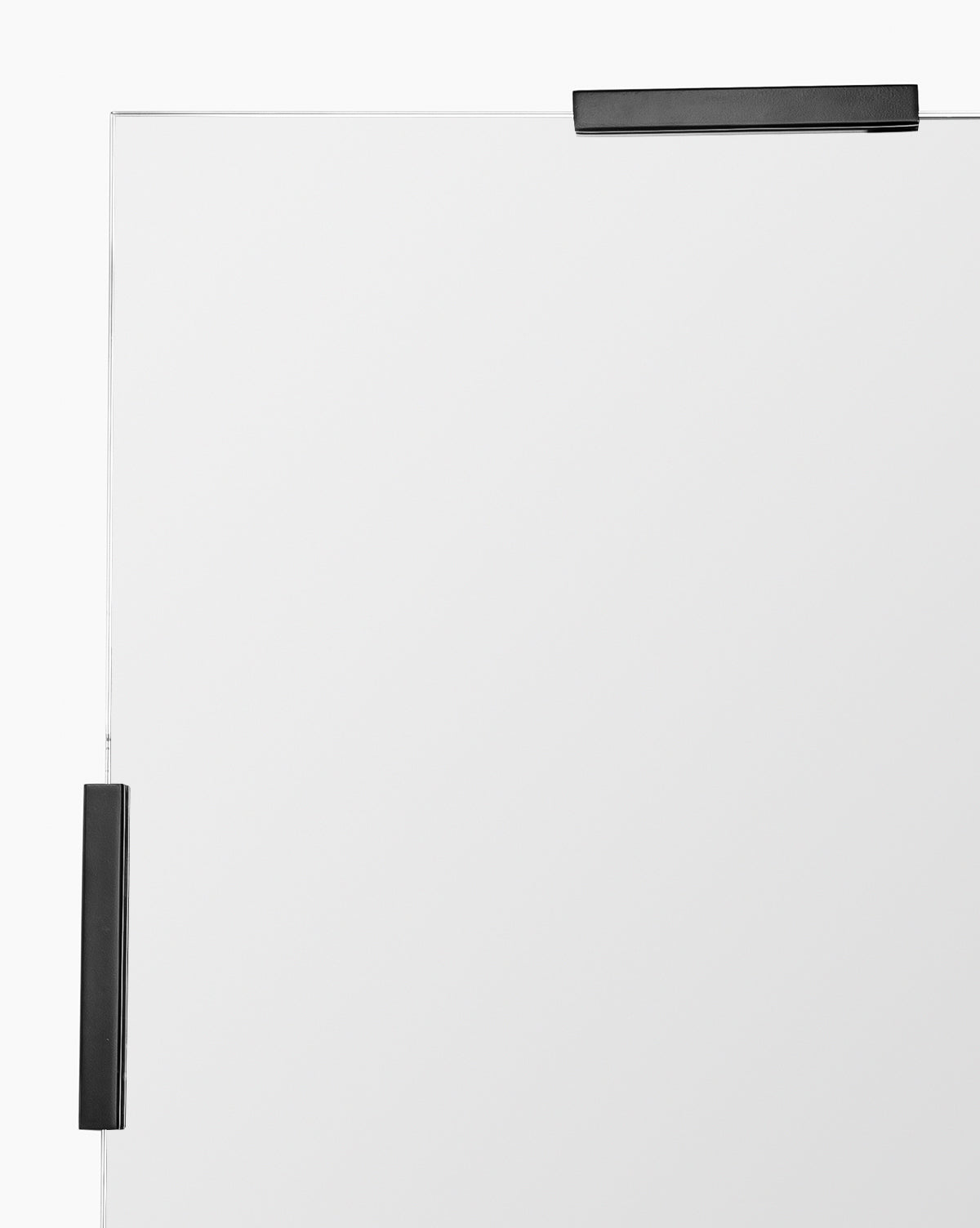 A close-up shows the top right corner of the Slade Mirror, a frameless design secured by two black metal brackets—one on the top and one on the right—against a white background, emphasizing its modern style, by Vendixs