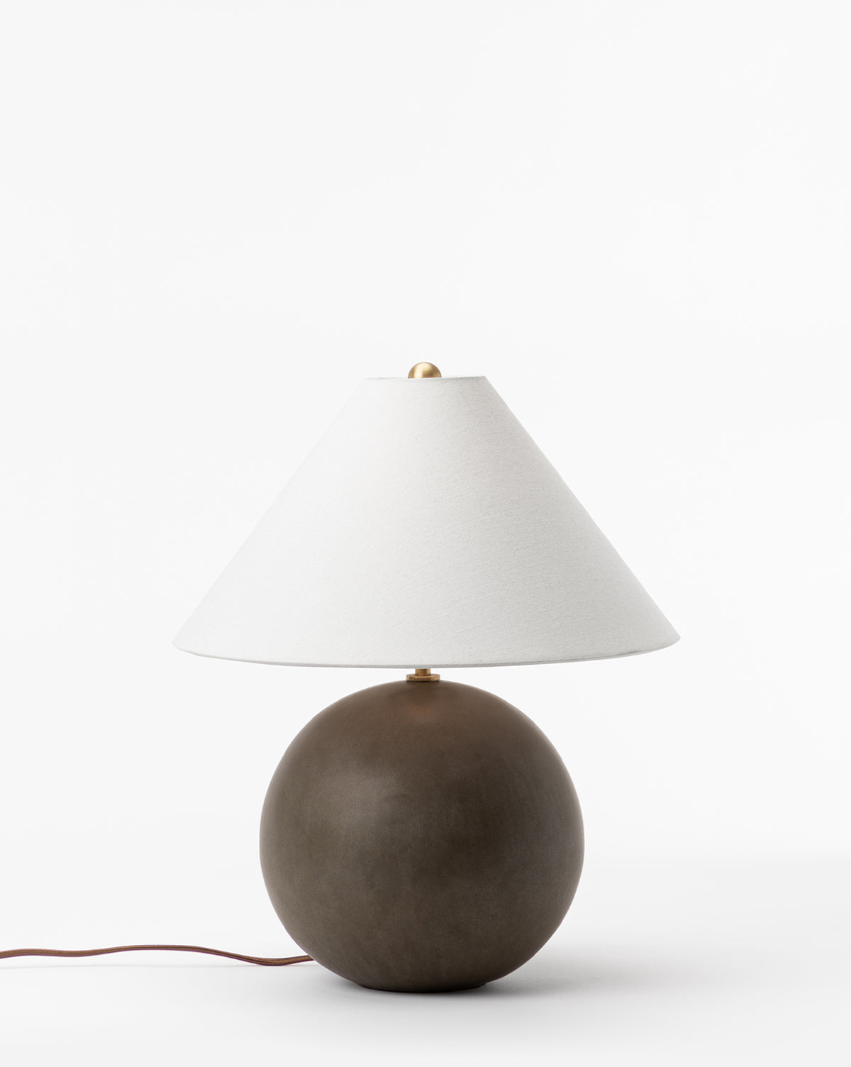 The Tess Ceramic Table Lamp features a round dark brown ceramic base and a wide conical white shade, set against a plain white background. A brown power cord extends from the base, by Vendixs