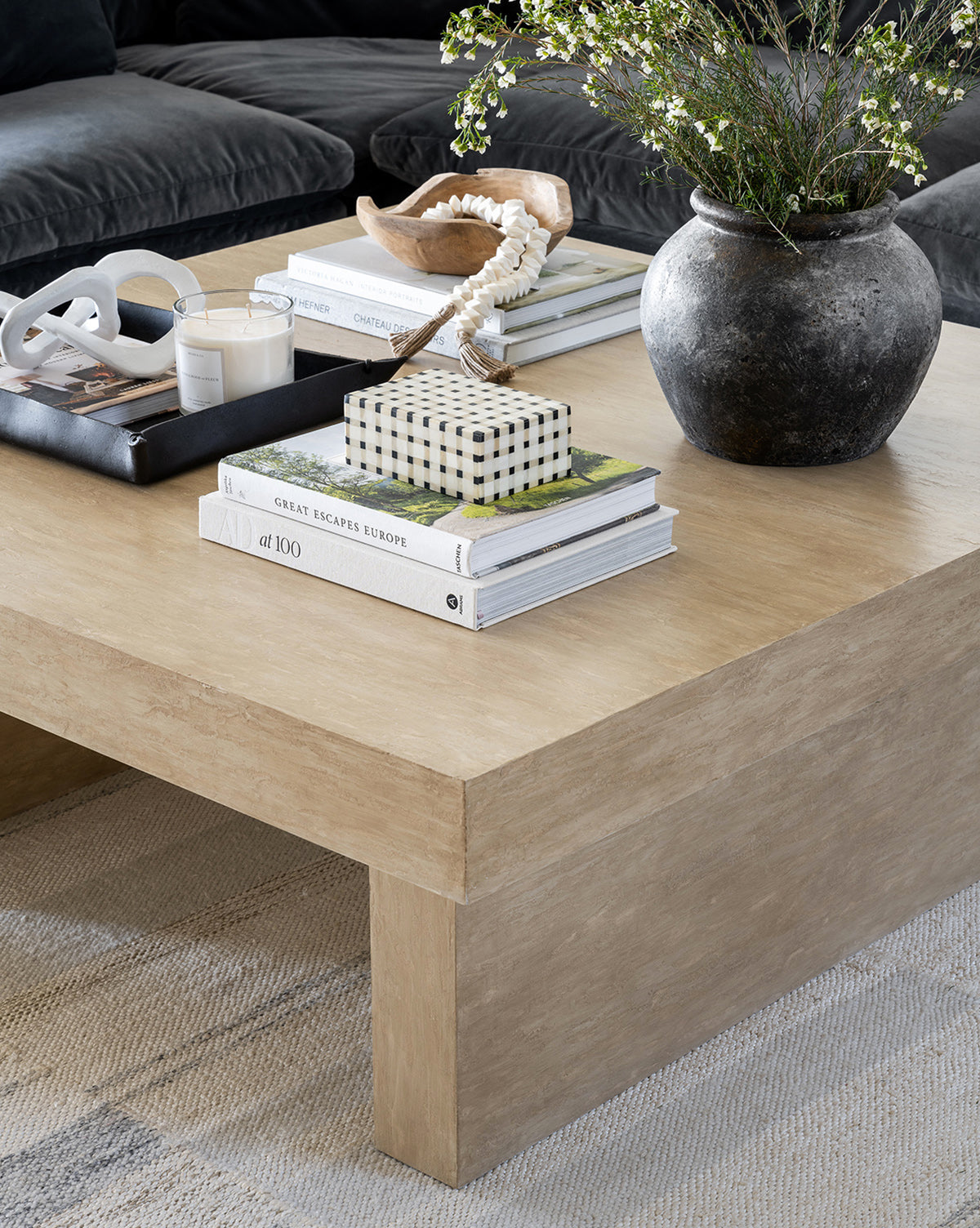 A wooden coffee table holds stacked books, a black vase with greenery, a candle, decorative beads, and the Grid Patterned Box. In the background, a dark sofa and textured rug complete the classic home decor look.