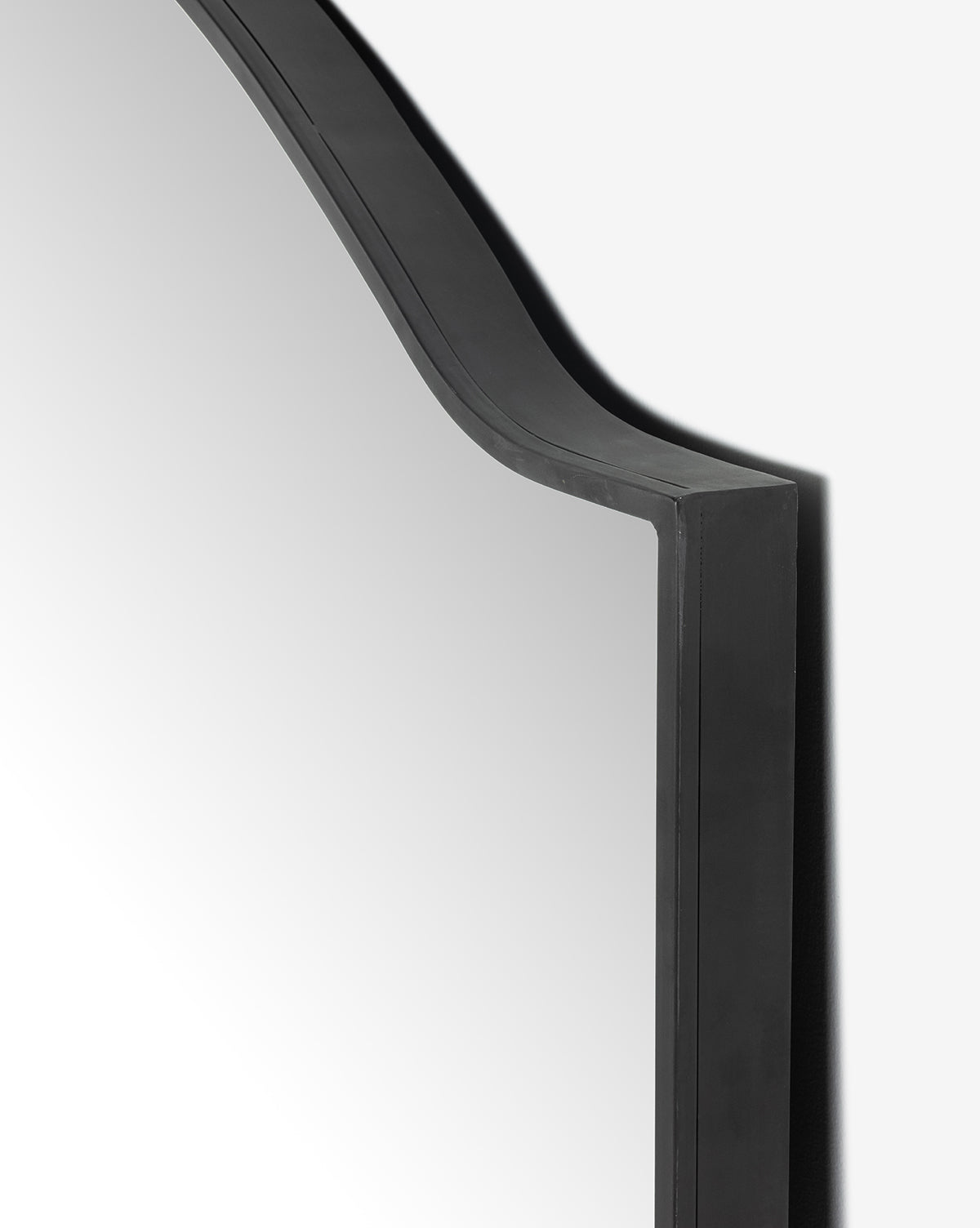 Close-up of the Willson Floor Mirror, featuring its arched top and black gunmetal frame, showing the left edge and part of the reflective surface against a plain white background, by Vendixs