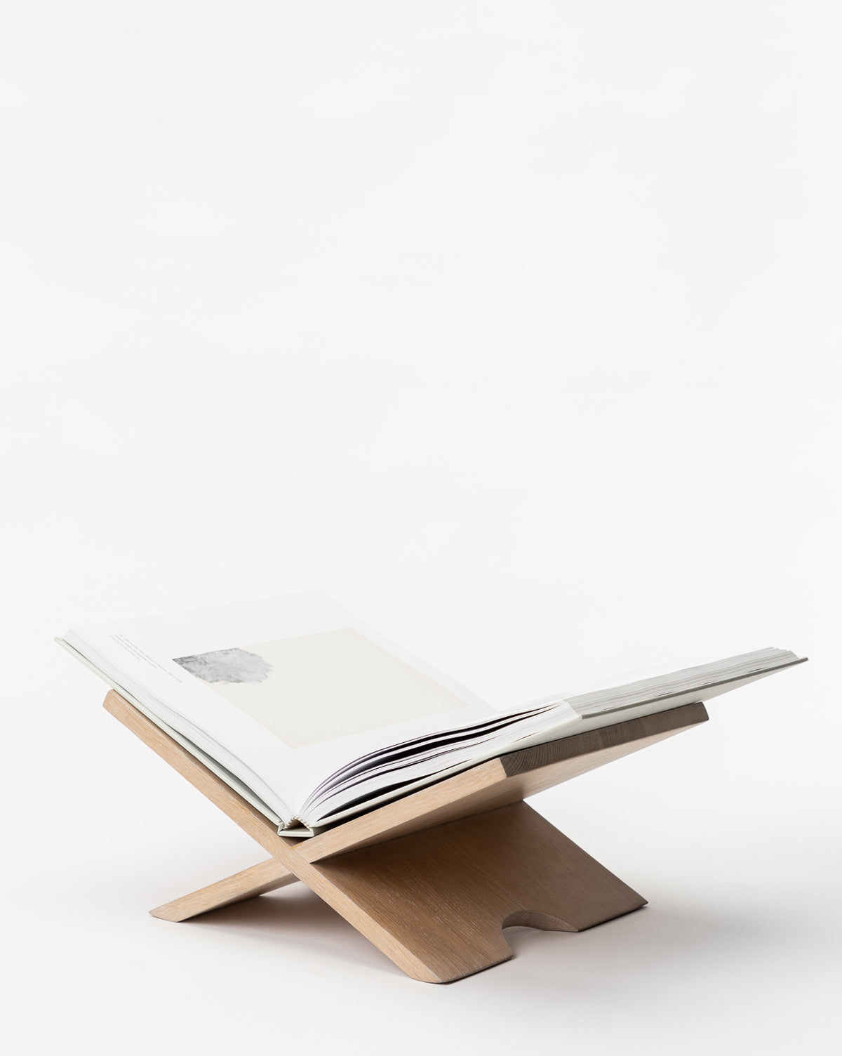 A Wooden Book Display made of minimalist oak forms an X shape with two interlocking panels, holding an open book against a plain white background.