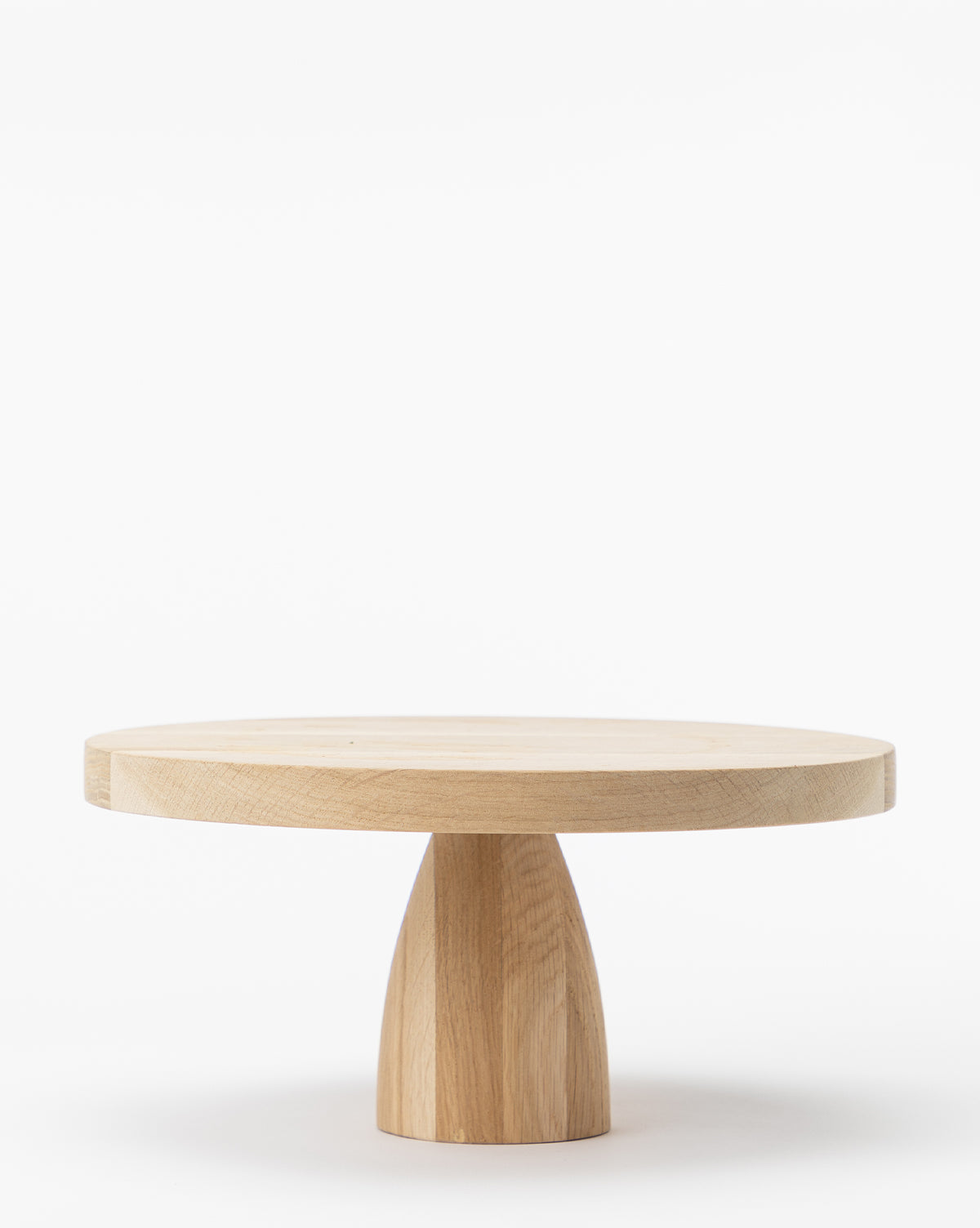 The Wooden Cake Stand features a round, light wood design with a thick top and sturdy, tapered base—ideal as a striking home decor piece or an oversized cake stand—shown on a plain white background, by Vendixs