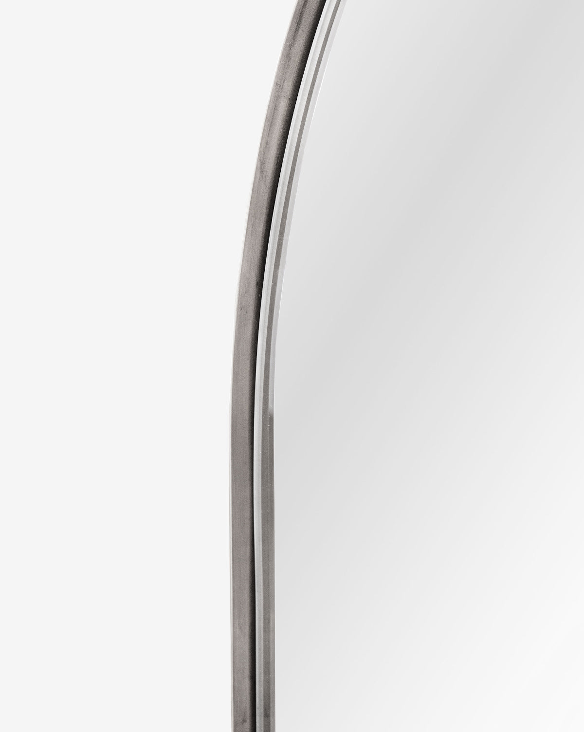 Close-up of the top left corner of the Wylie Arched Mirror, featuring a rounded metal frame and shatterproof glass, set against a plain white background, by Vendixs