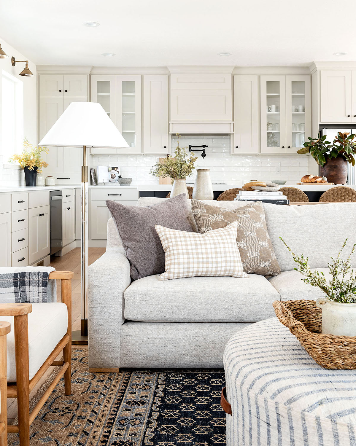 A bright, airy living room and kitchen with light cabinets, a neutral sofa, wooden accents, decorative plants, and the Anya Indigo Hand-Knotted Wool Rug creates a cozy, modern farmhouse vibe, by Vendixs