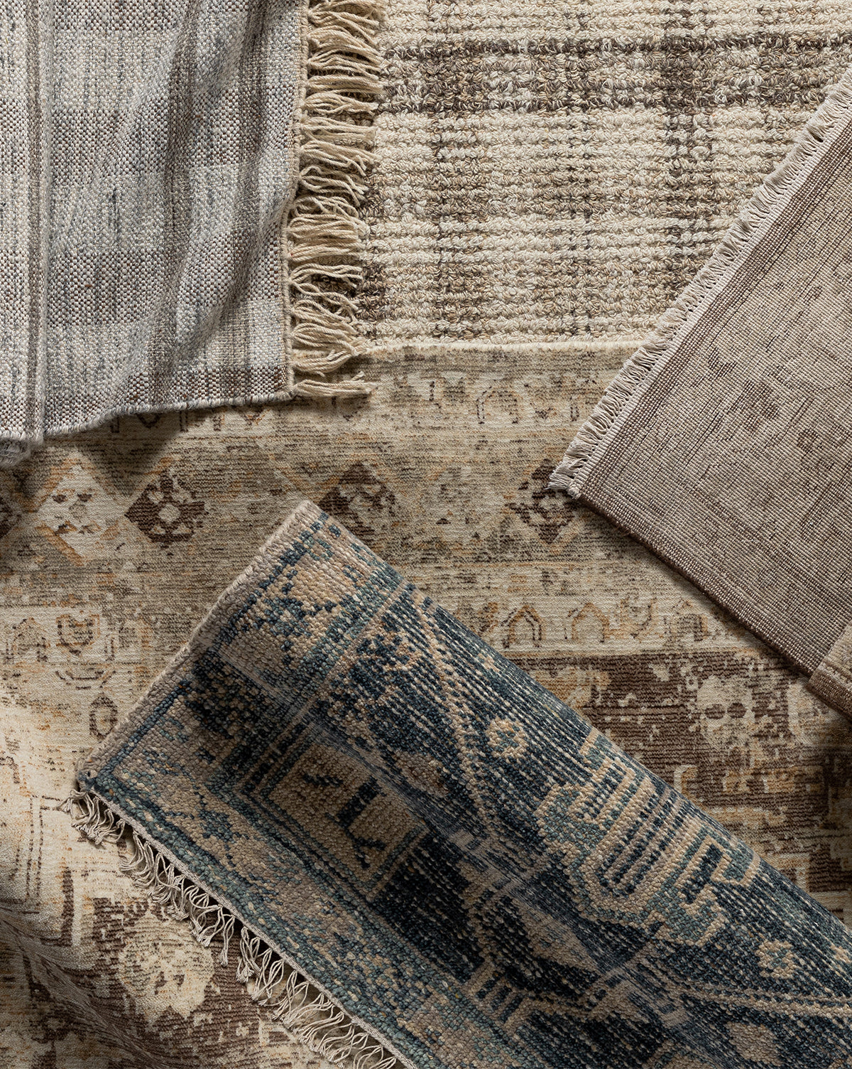 A top-down view of four overlapping Marcella Handwoven Rugs in neutral and blue tones, featuring unique patterns and fringed edges, including a wool blend and a neutral tan option, all arranged on a textured surface, by Vendixs