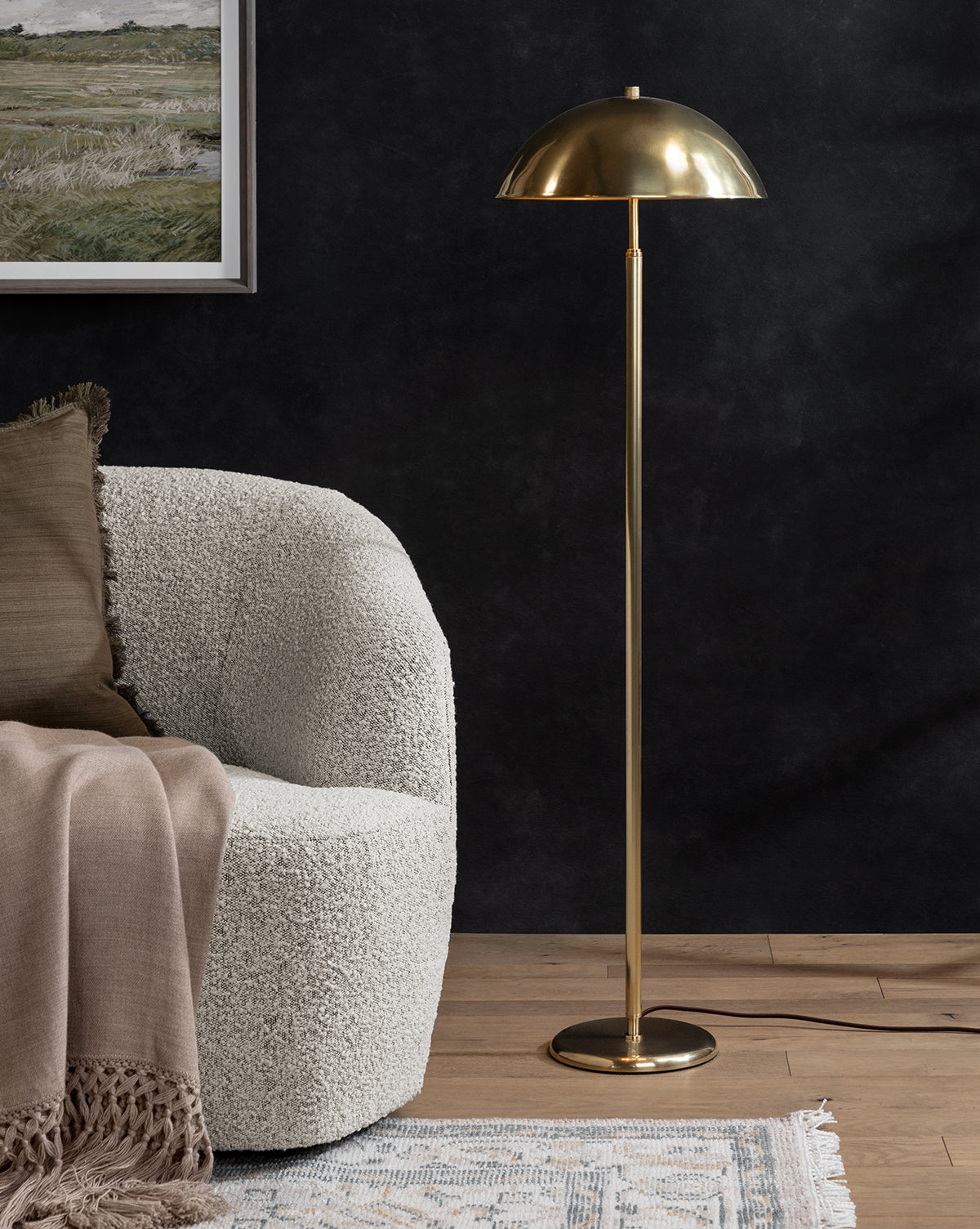 A modern living room with a textured white armchair, beige throw blanket, the Aldorno Floor Lamp featuring a dome-shaped shade, a blue patterned rug, and a framed landscape painting on a dark wall, by Vendixs